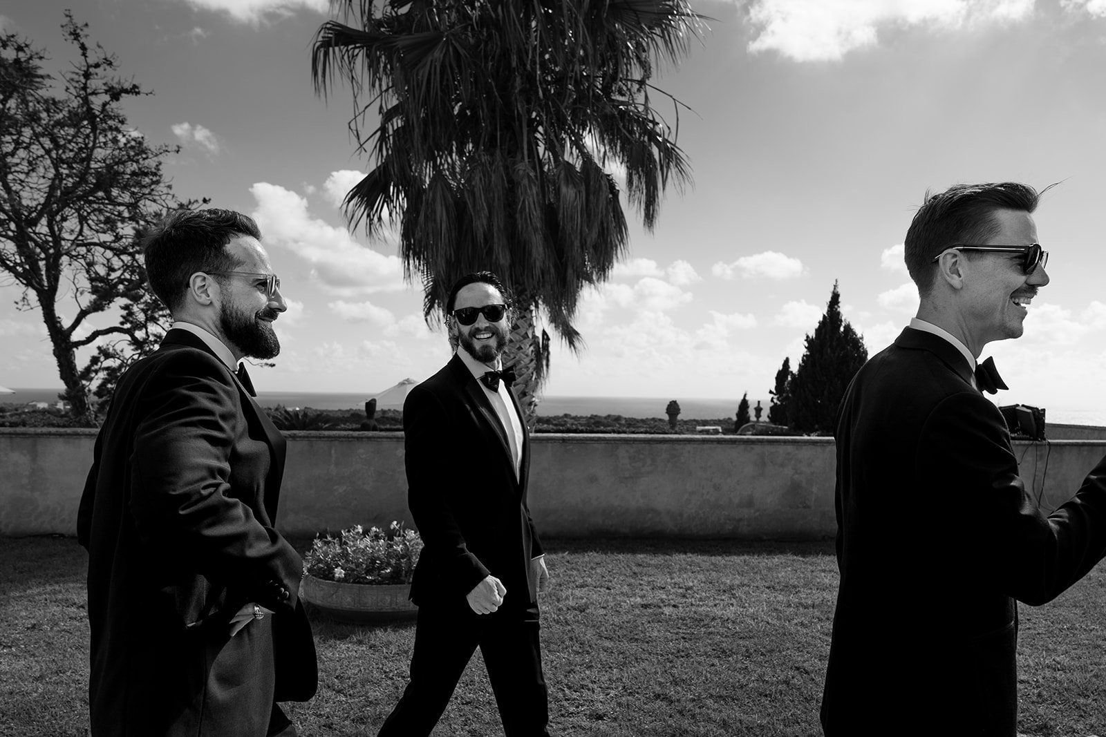Black and white candid moment of groomsmen walking and laughing at a Mediterranean villa wedding