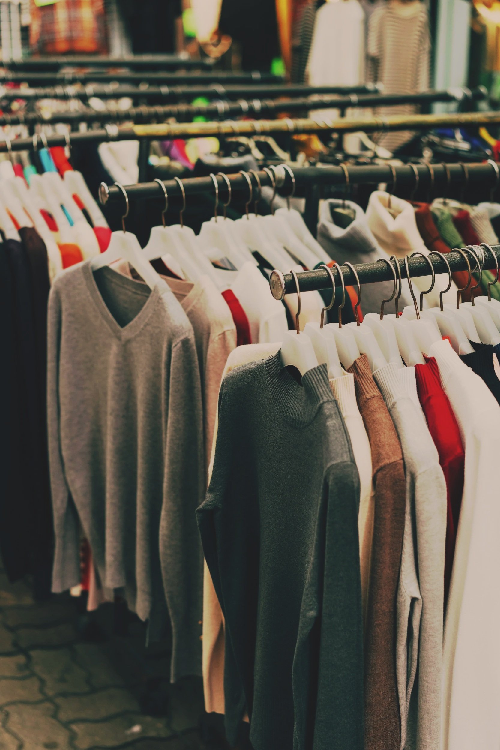 Clothing racks filled with various sweaters and shirts in a thrift store or clothing store.