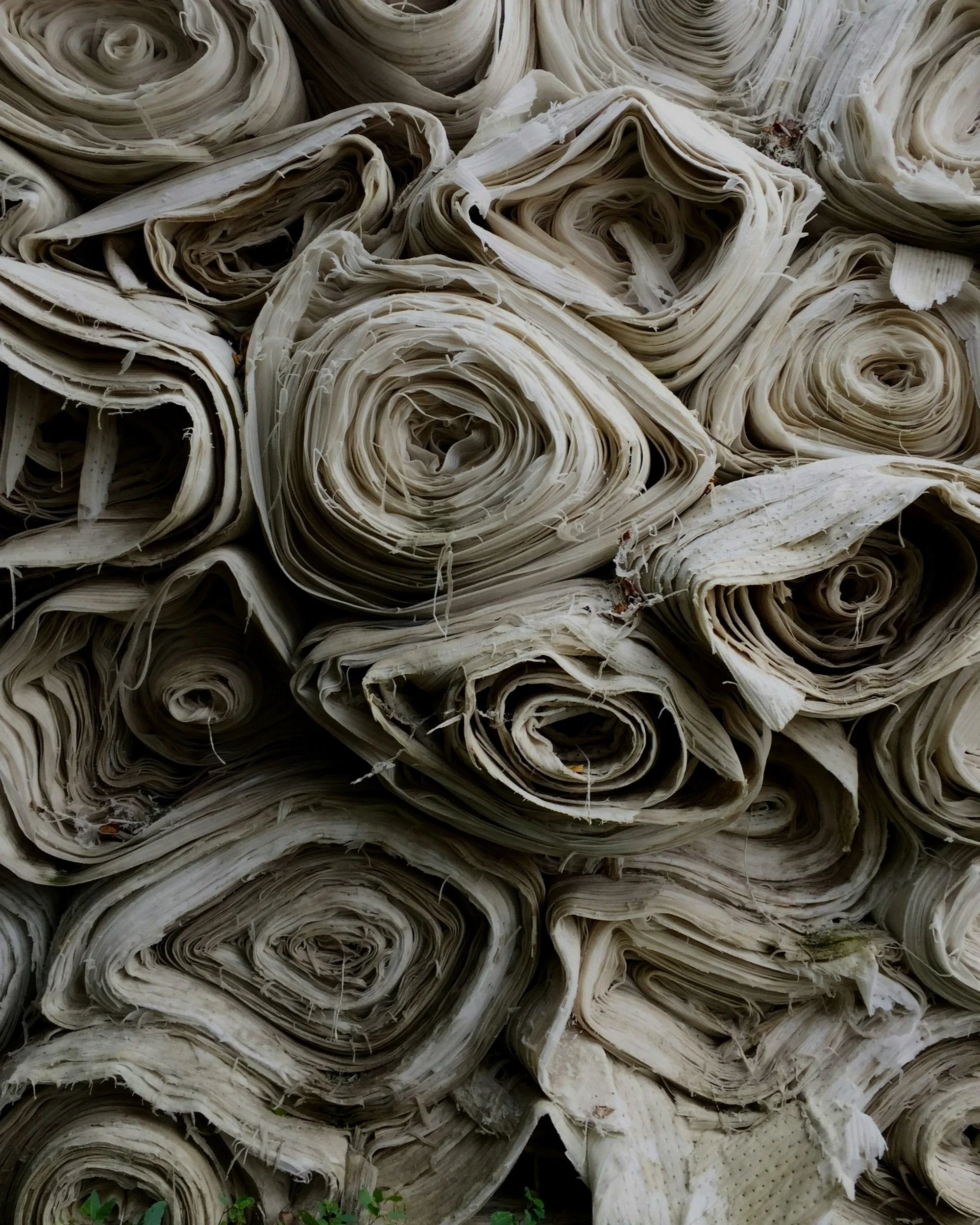 A stack of tightly rolled, brown paper sheets or parchment paper rolls.