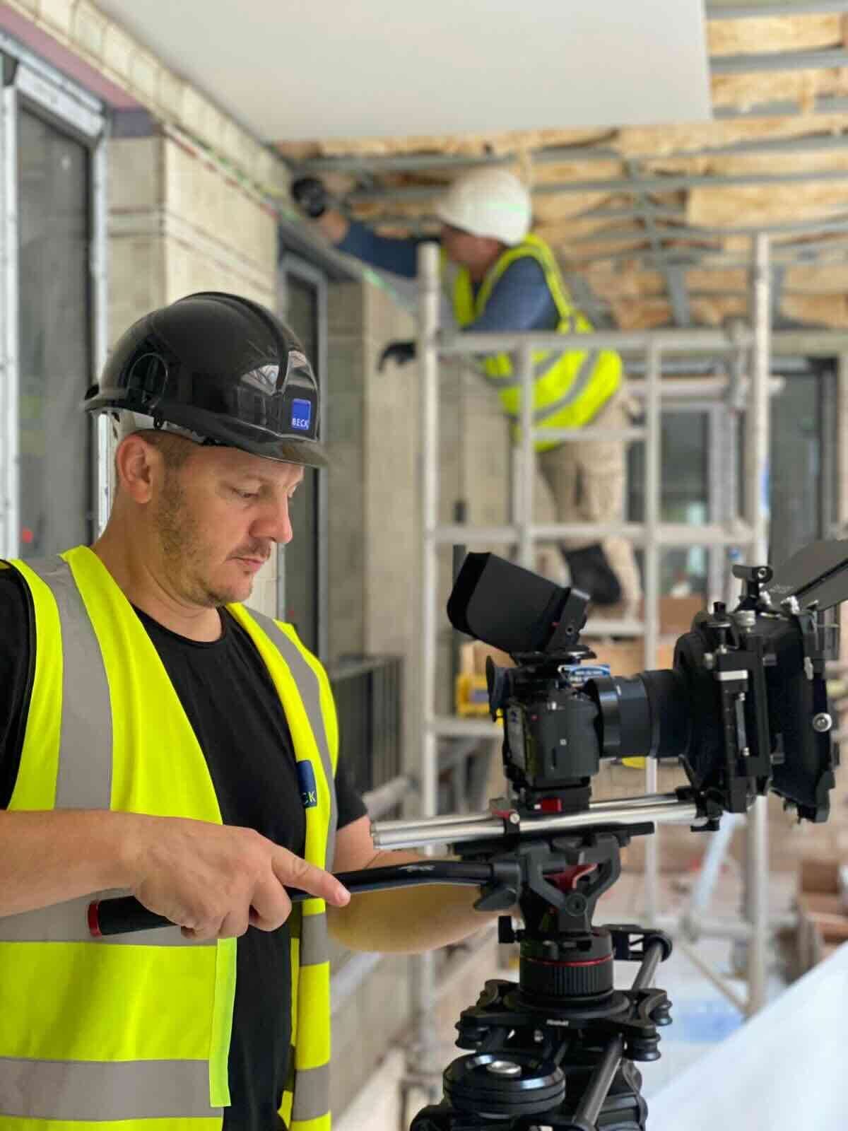 A camera operator in hard hat and hi-vis on a construction site