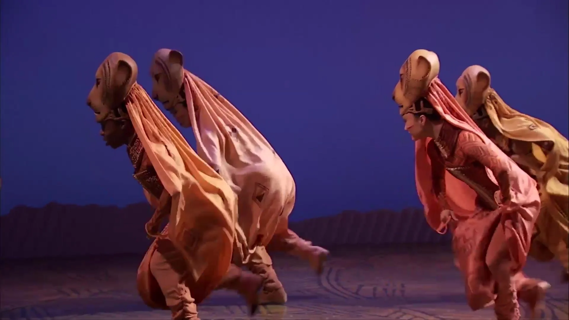 Lioness dancers in flowing orange costumes on stage in The Lion King