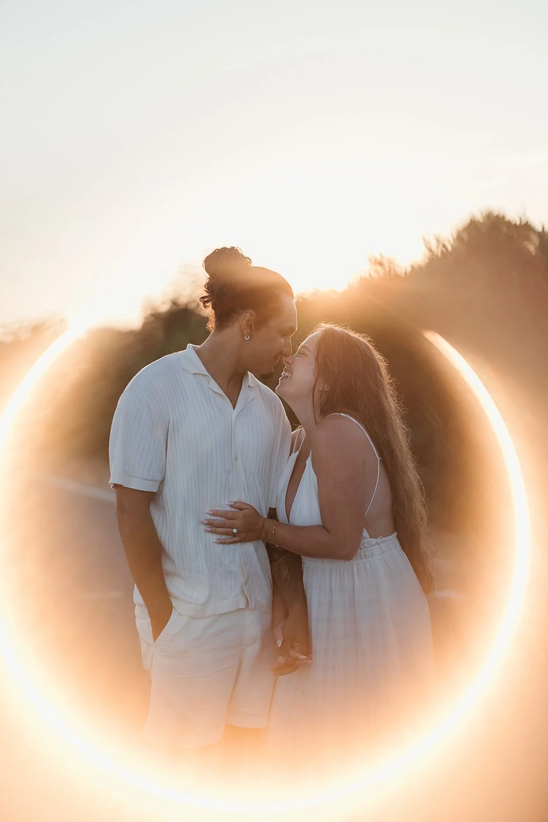 A couple smiles and embraces outdoors at sunset, glowing in a warm light ring—captured by a Portugal wedding photographer.