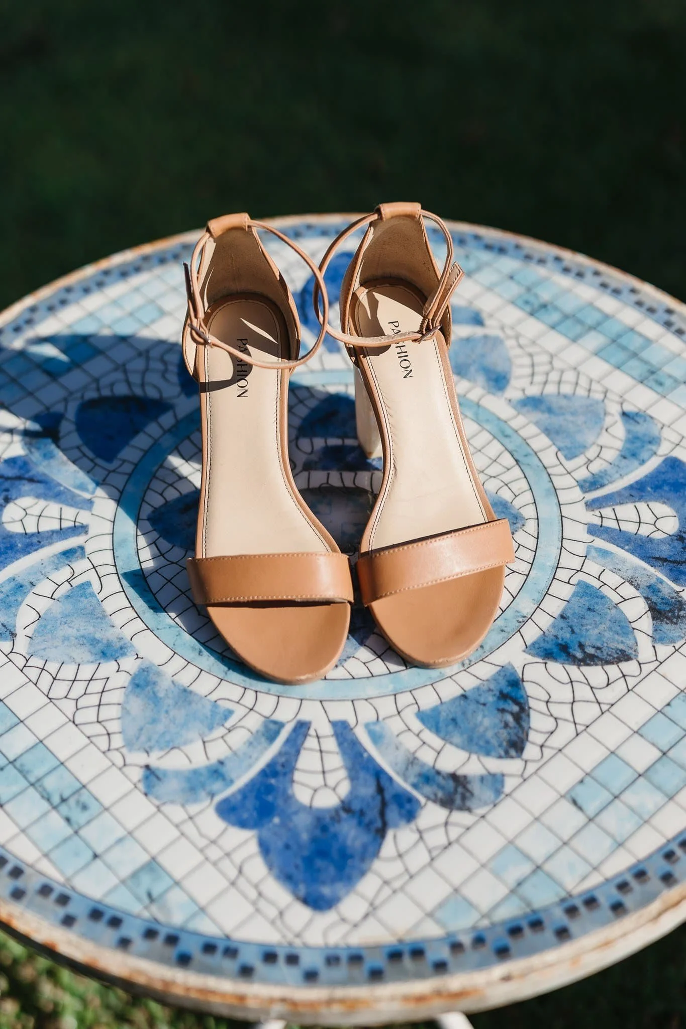 A pair of tan high-heeled sandals placed on a decorative blue and white tiled table outdoors.