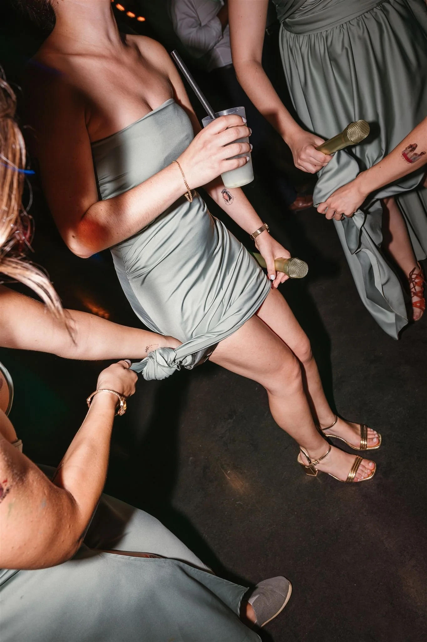 Emotional wedding moment in Portugal: People dancing at a party, wearing matching satin dresses in a light grayish-green color, holding microphones, with one person holding a drink.
