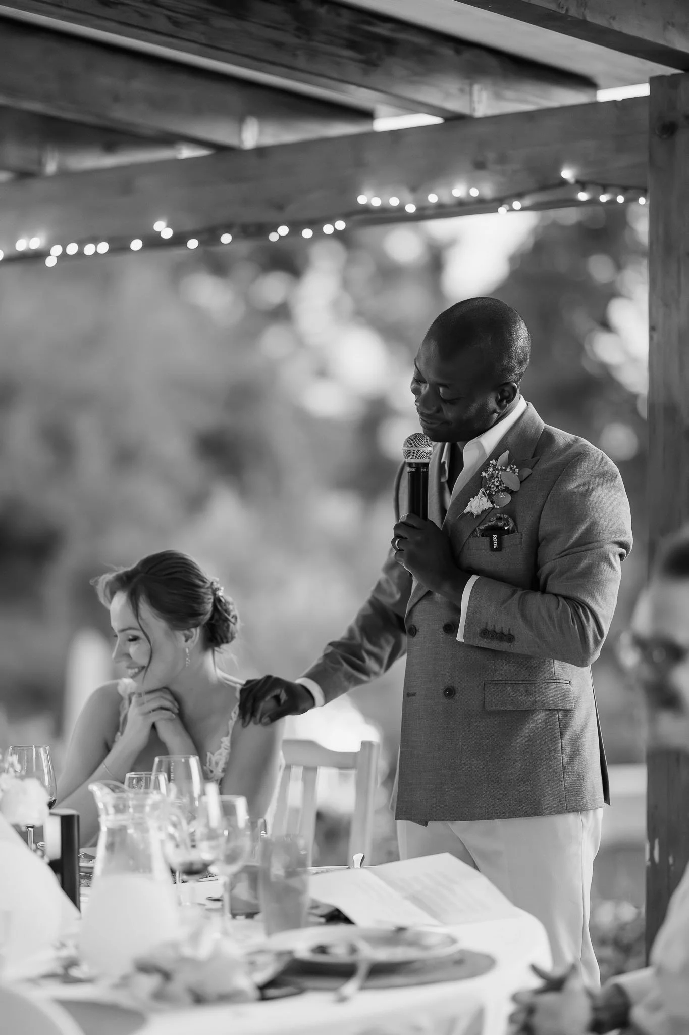 A Portugal wedding photographer captures a groom giving a speech while holding his bride’s hand at an outdoor reception.