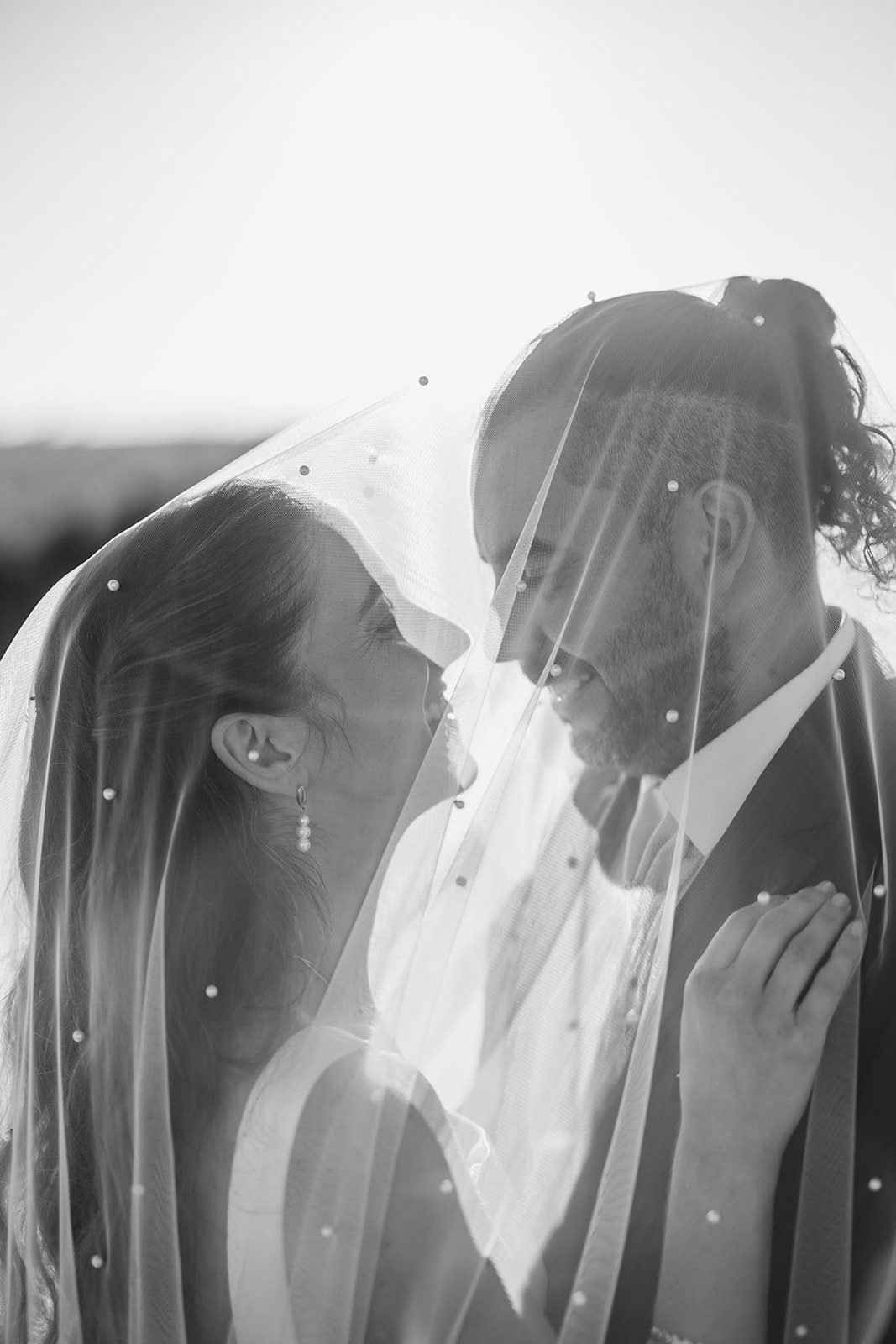 A bride and groom smile at each other under a wedding veil, bathed in sunlight—Portugal Wedding Photography captures the magic.