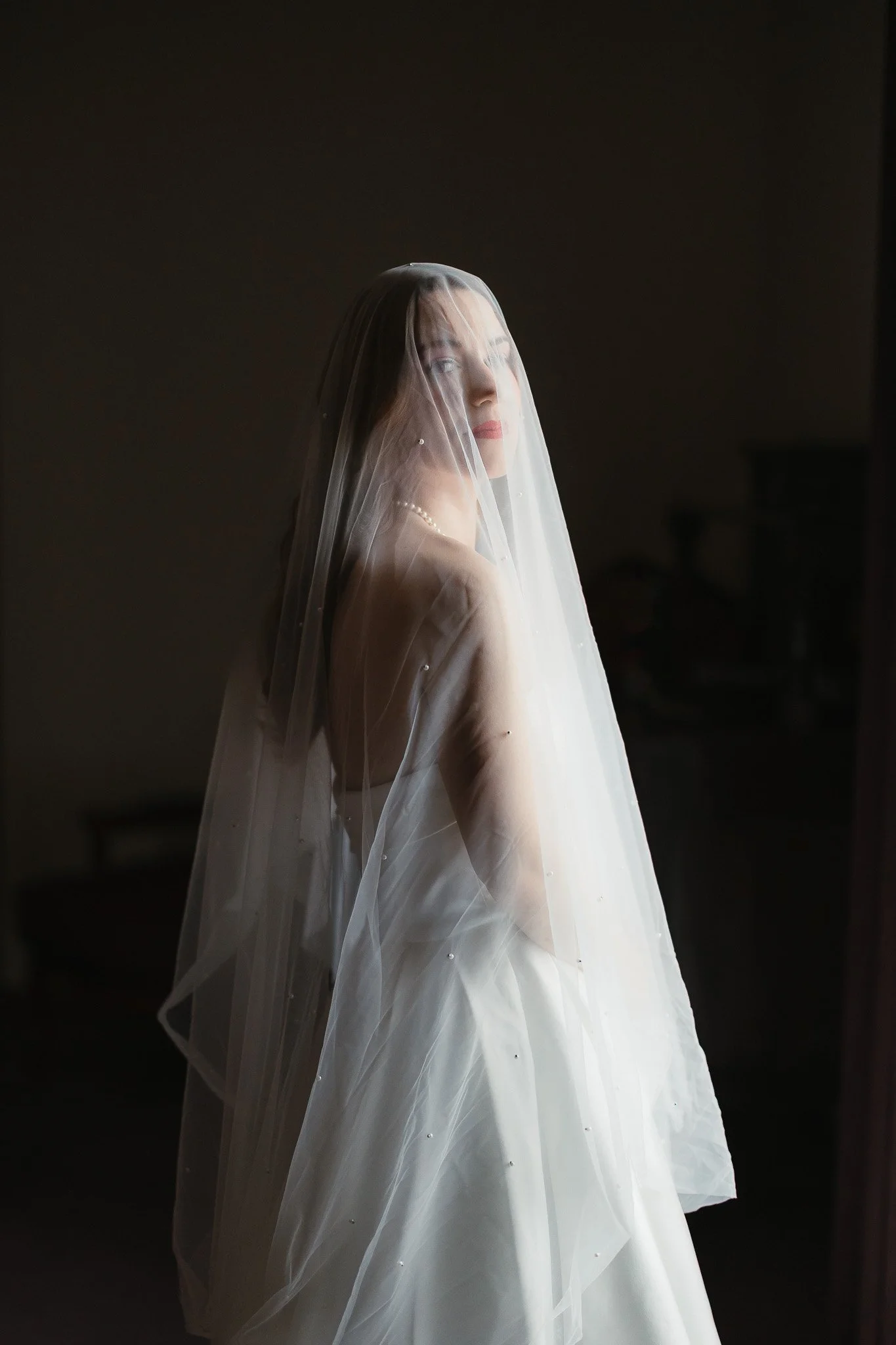 A bride in a white gown and veil stands in soft light, captured with timeless elegance by Portugal Wedding Photography.
