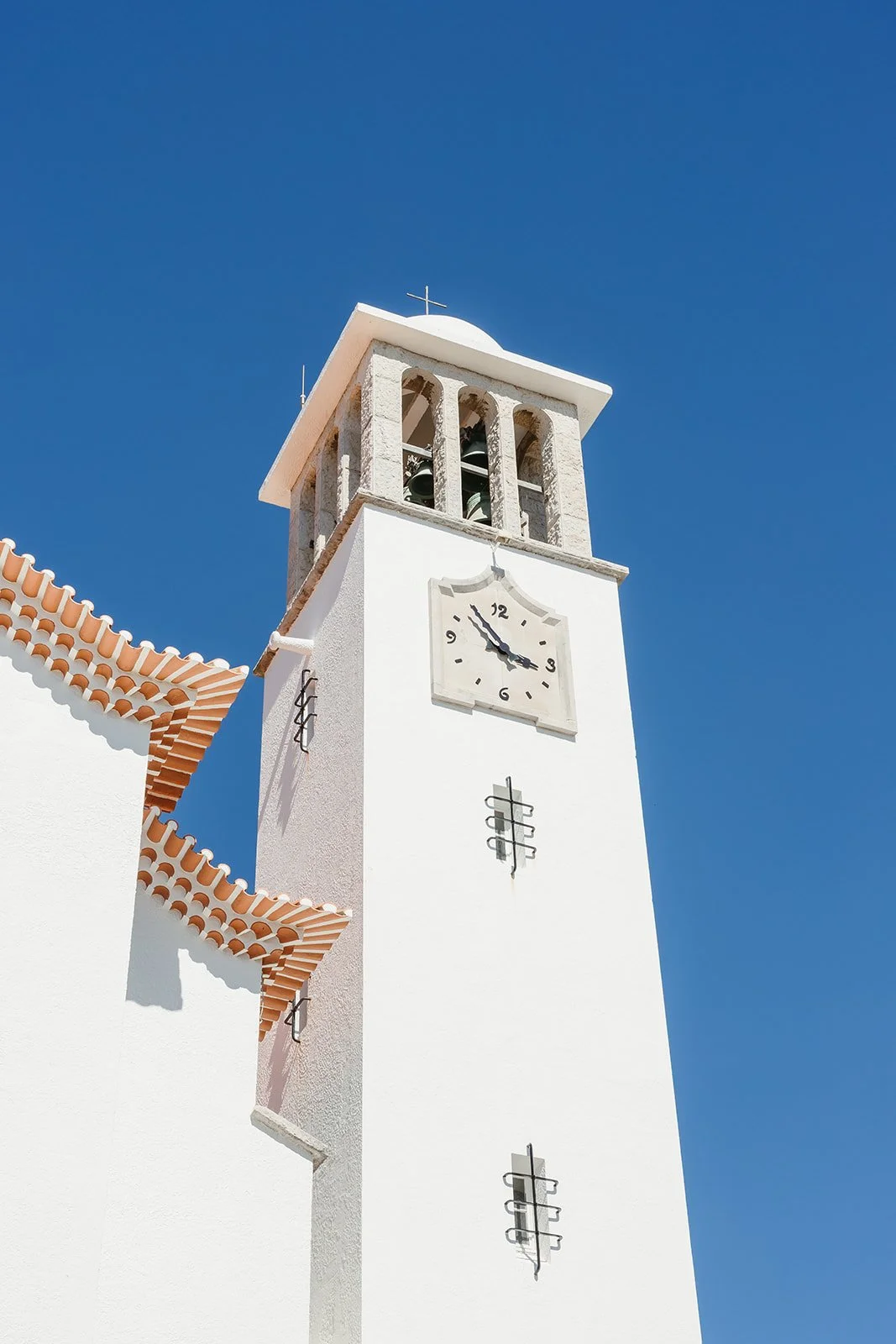 White clock tower with a bell and tiled roof, perfect for Portugal wedding photography, set against a clear blue sky.