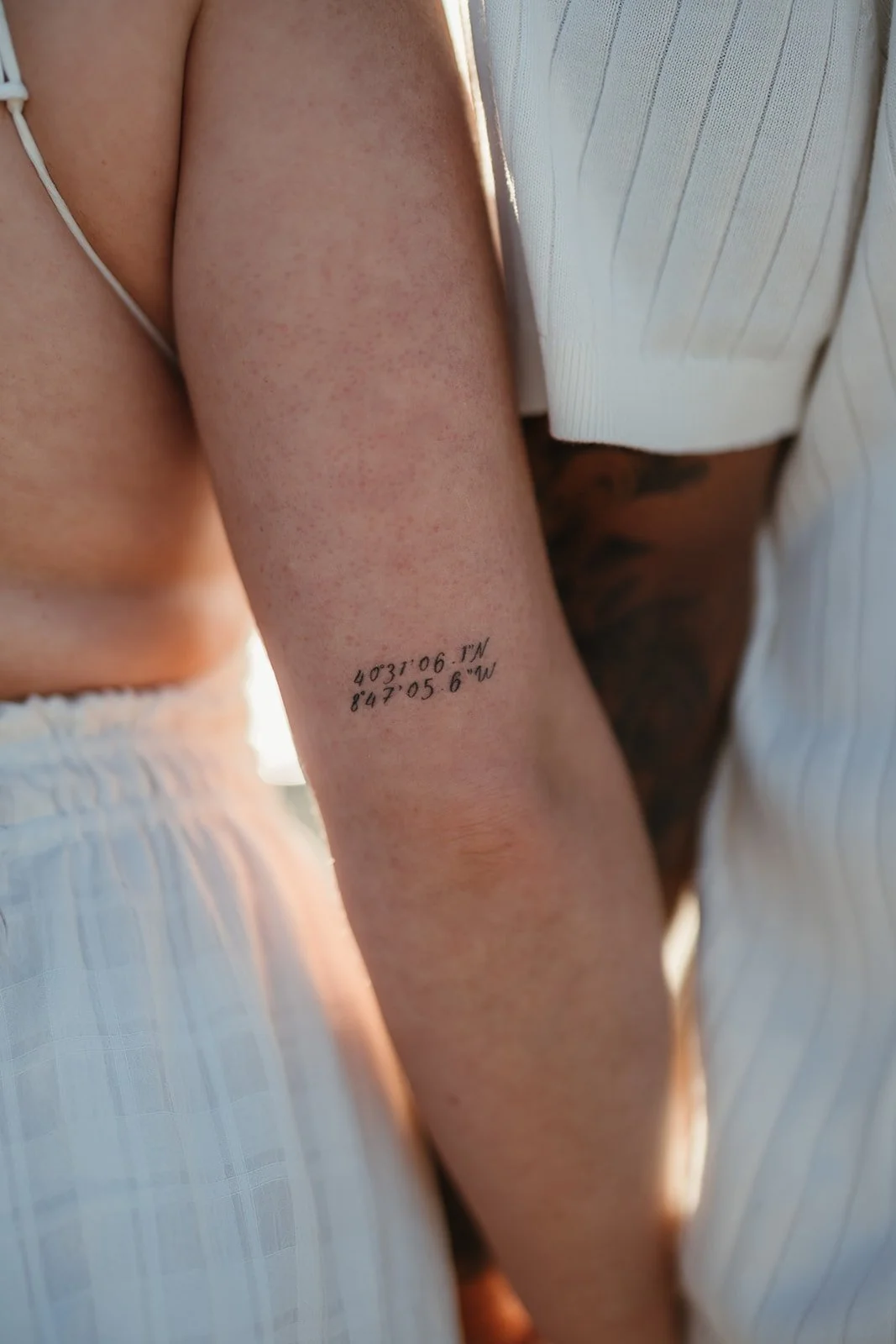 A close-up of a person's arm with a coordinates tattoo, standing next to another in white—captured by a Portugal Wedding Photographer.