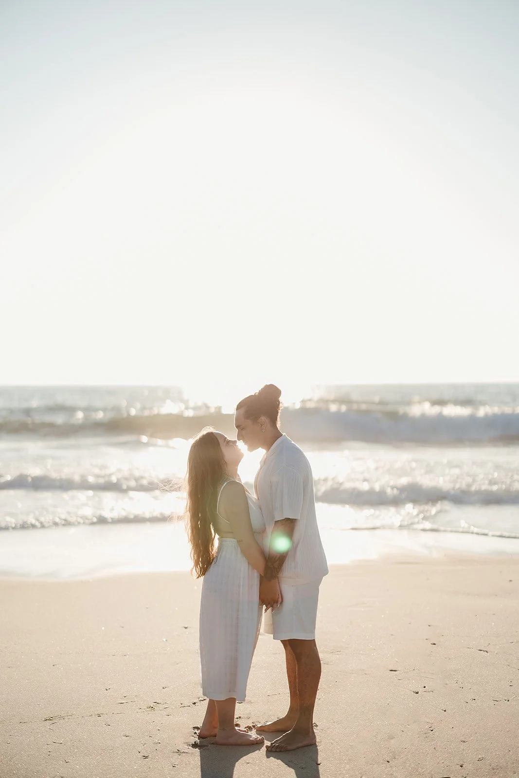 A couple holds hands and kisses on a sunny beach, captured perfectly by a Portugal wedding photographer.