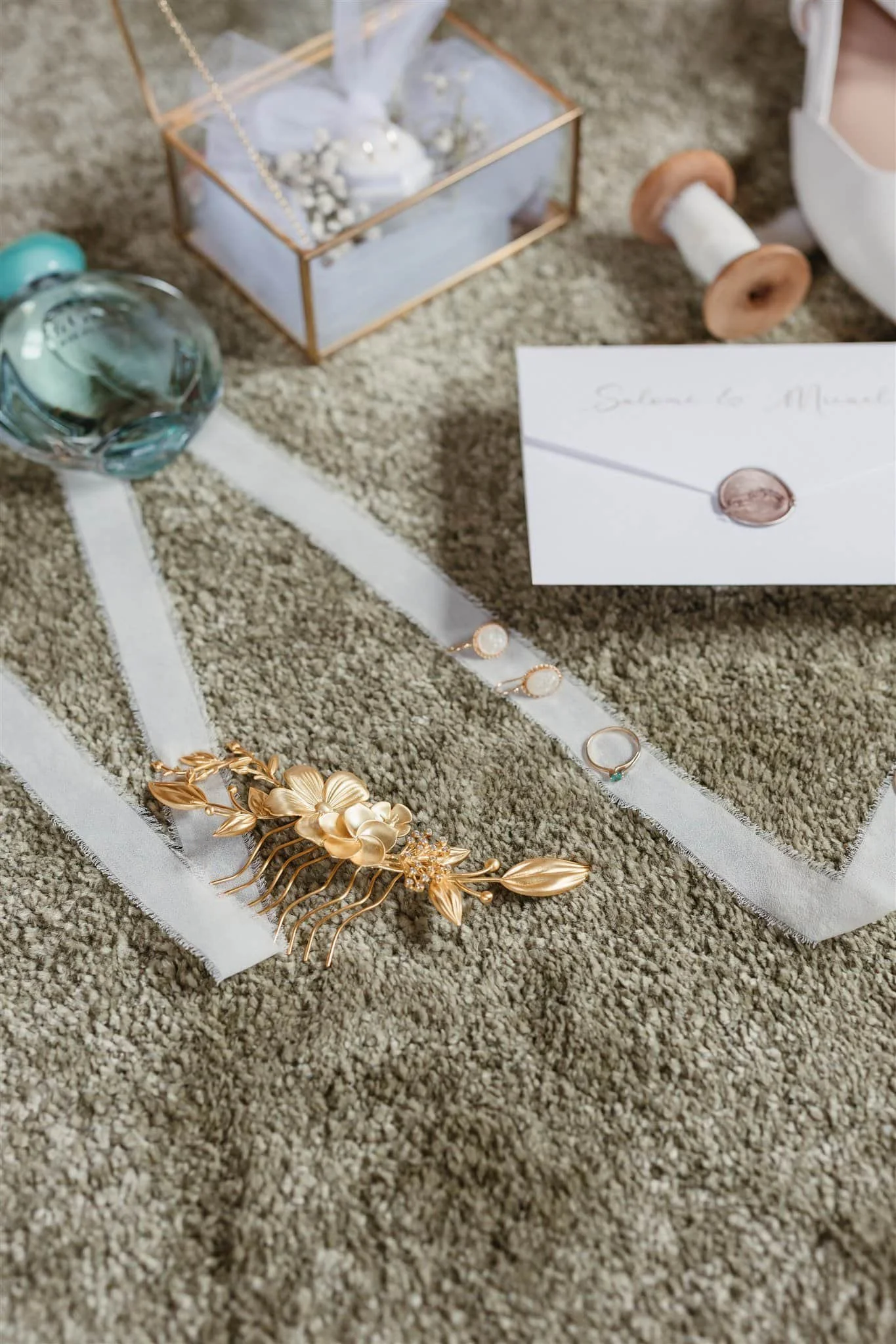 Gold floral hairpiece, perfume, rings, and ribbon styled on green for a flat lay by a Portugal Wedding Photographer.