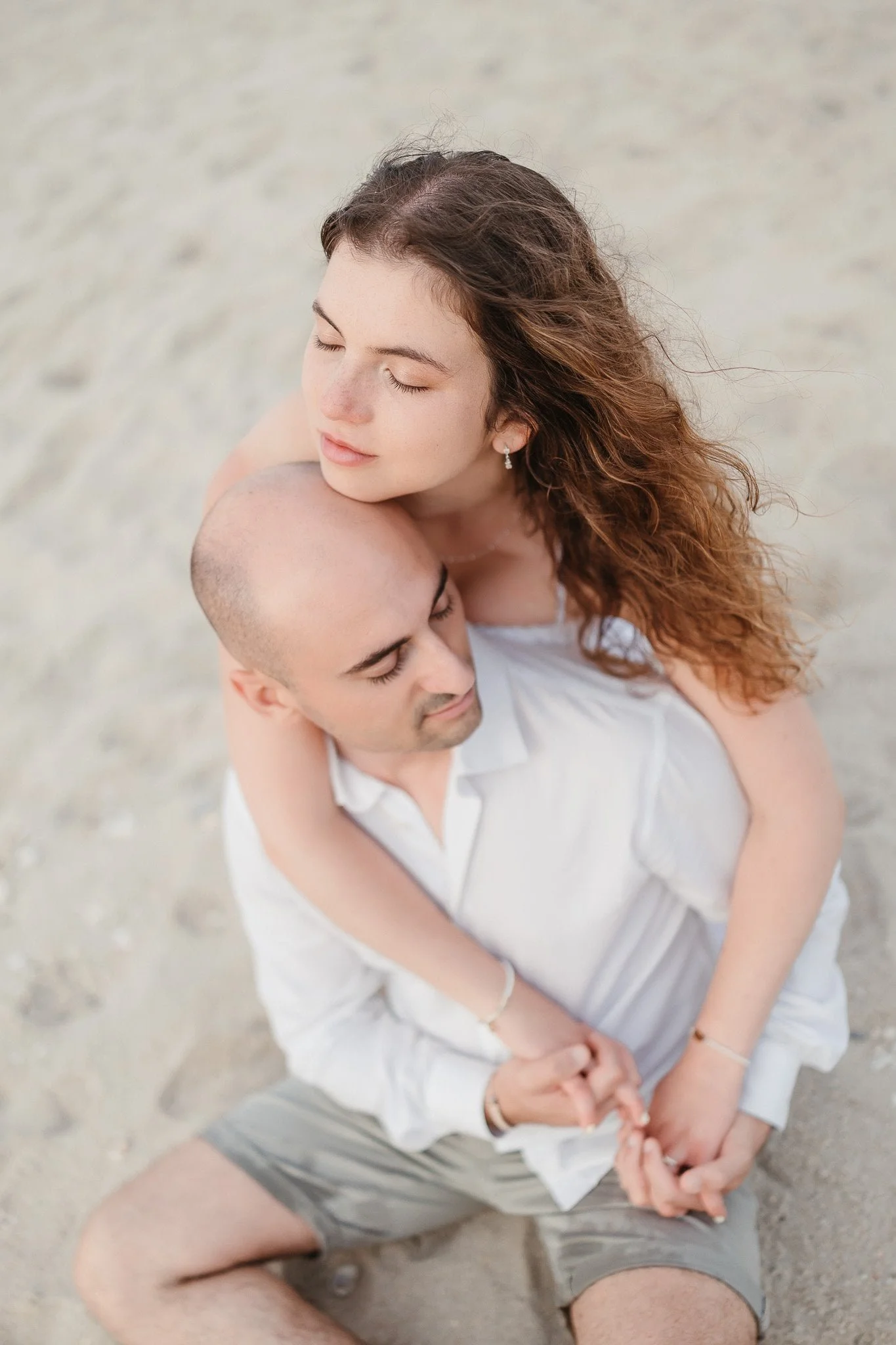 Elopment Photographer: A couple sitting on the sand at the beach, embracing each other with their eyes closed.