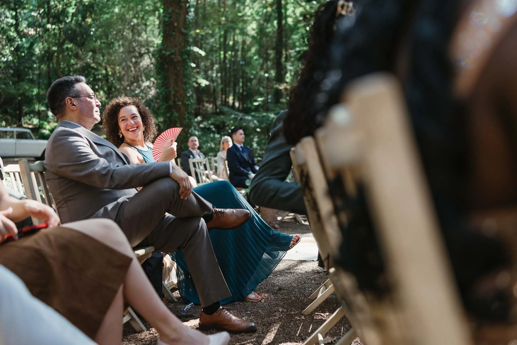 A woman in a blue dress smiles and fans herself beside a man at an outdoor event, captured by a Portugal Wedding Photographer.