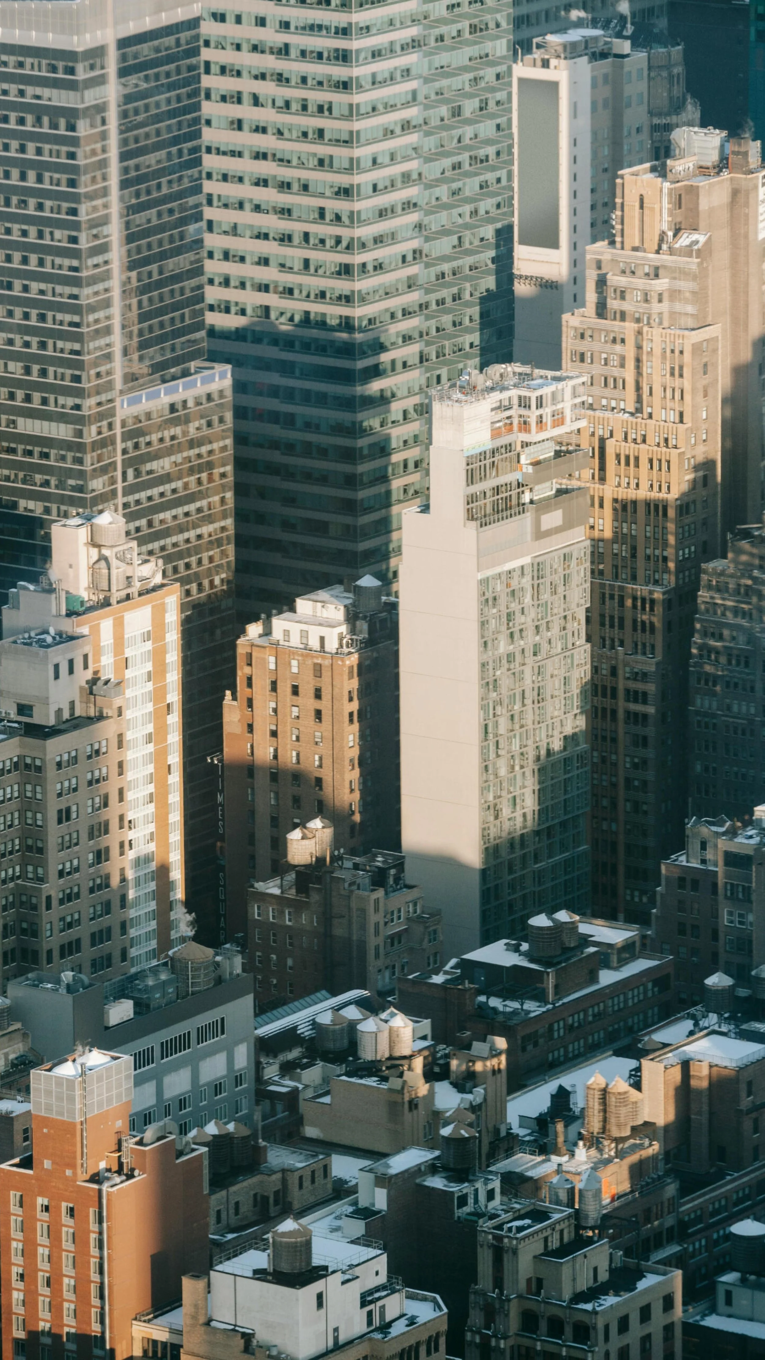 Vue d'en haut de nombreux gratte-ciel de ville avec des bâtiments modernes en verre et en pierre, certains ont des toits plats avec des installations techniques. Il y a de la neige sur certains toits.