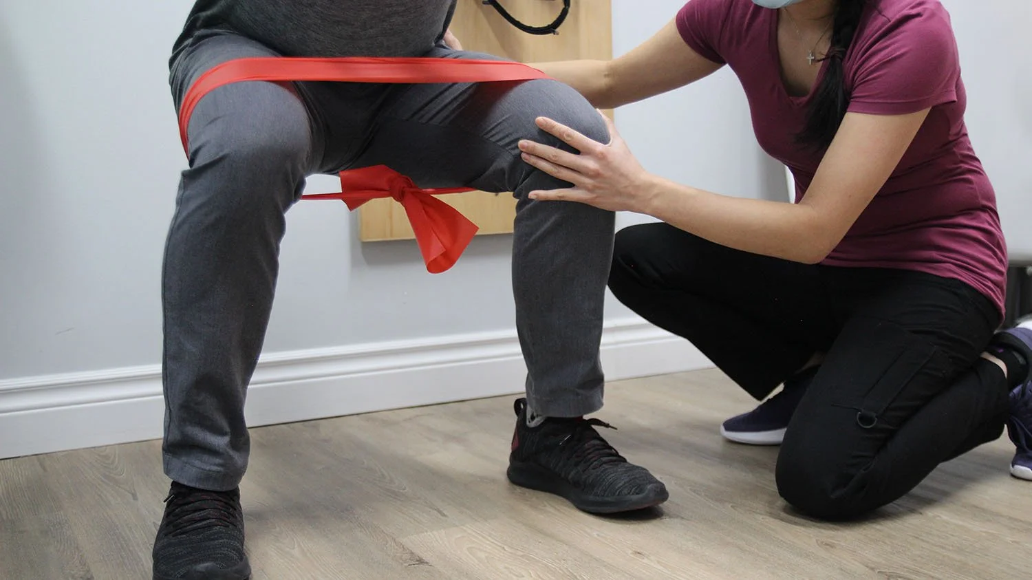 A person undergoing physical therapy or assessment while sitting on a chair, with a healthcare provider supporting and examining their knee.