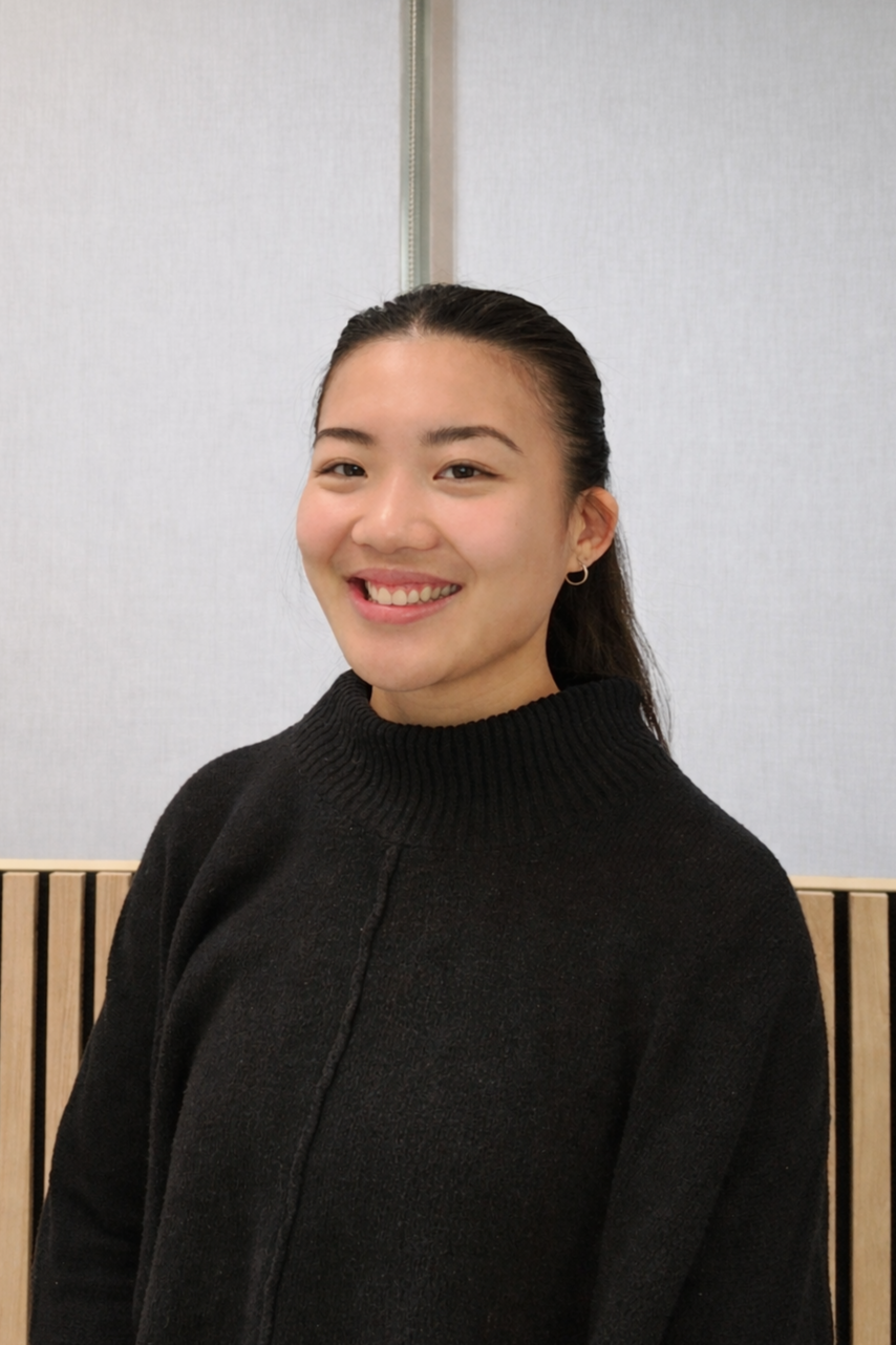 A young woman with long dark hair tied back, wearing a black turtleneck sweater, smiling in front of a light-colored wall.