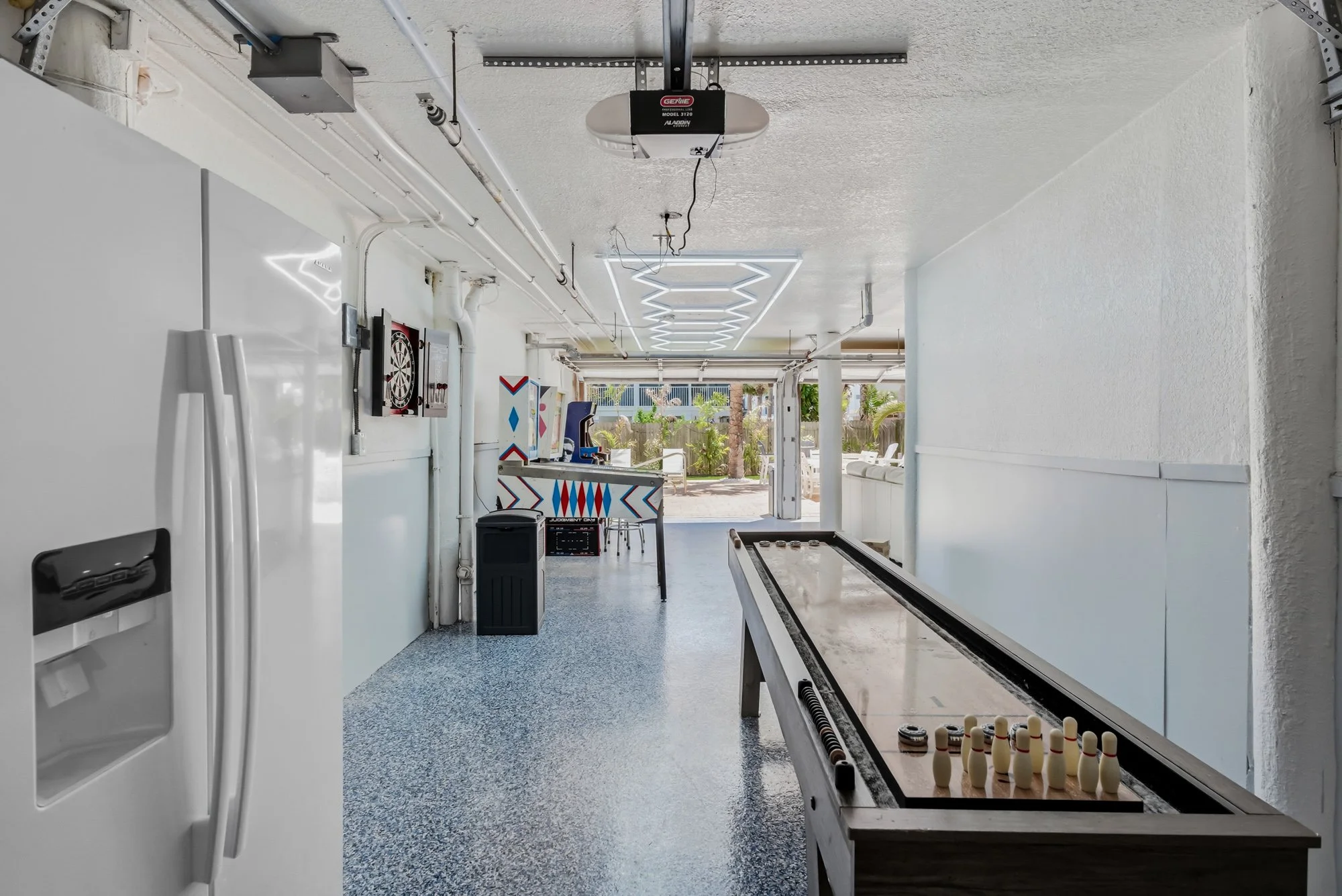 Shuffleboard table and refrigerator in game room.