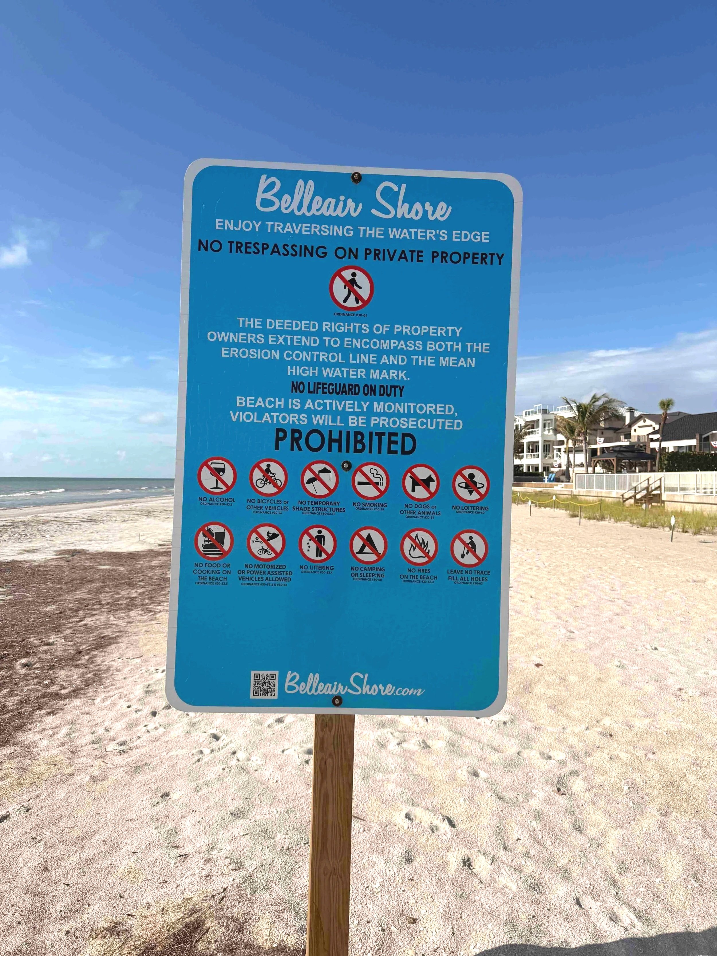 Belleair Shore beach sign inviting visitors to walk the water's edge while warning against trespassing on private beachfront property.