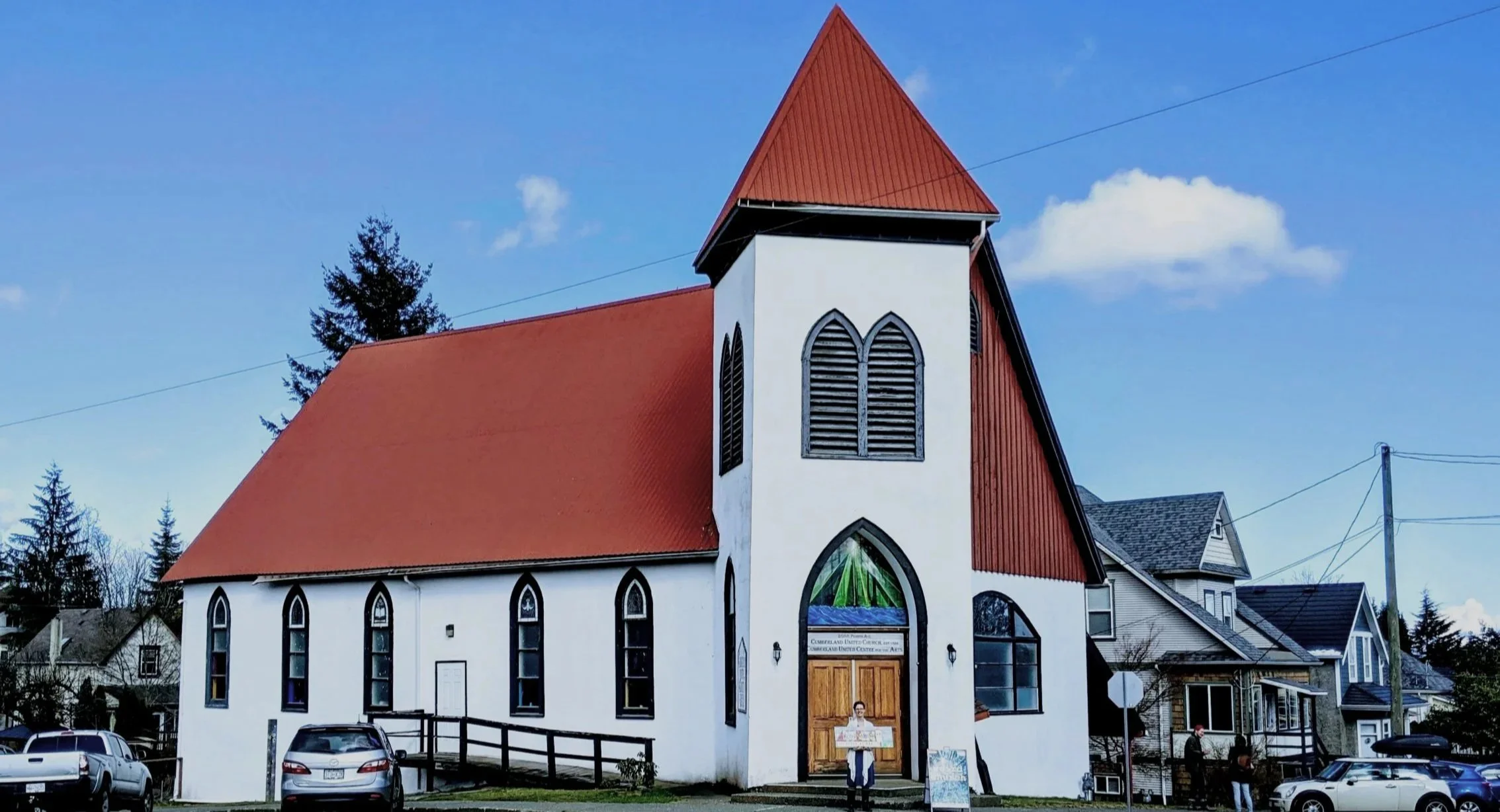 Weird Church, based in Cumberland BC and established in 2018. A white church with a red steeple and roof, stained glass windows, and wooden doors.
