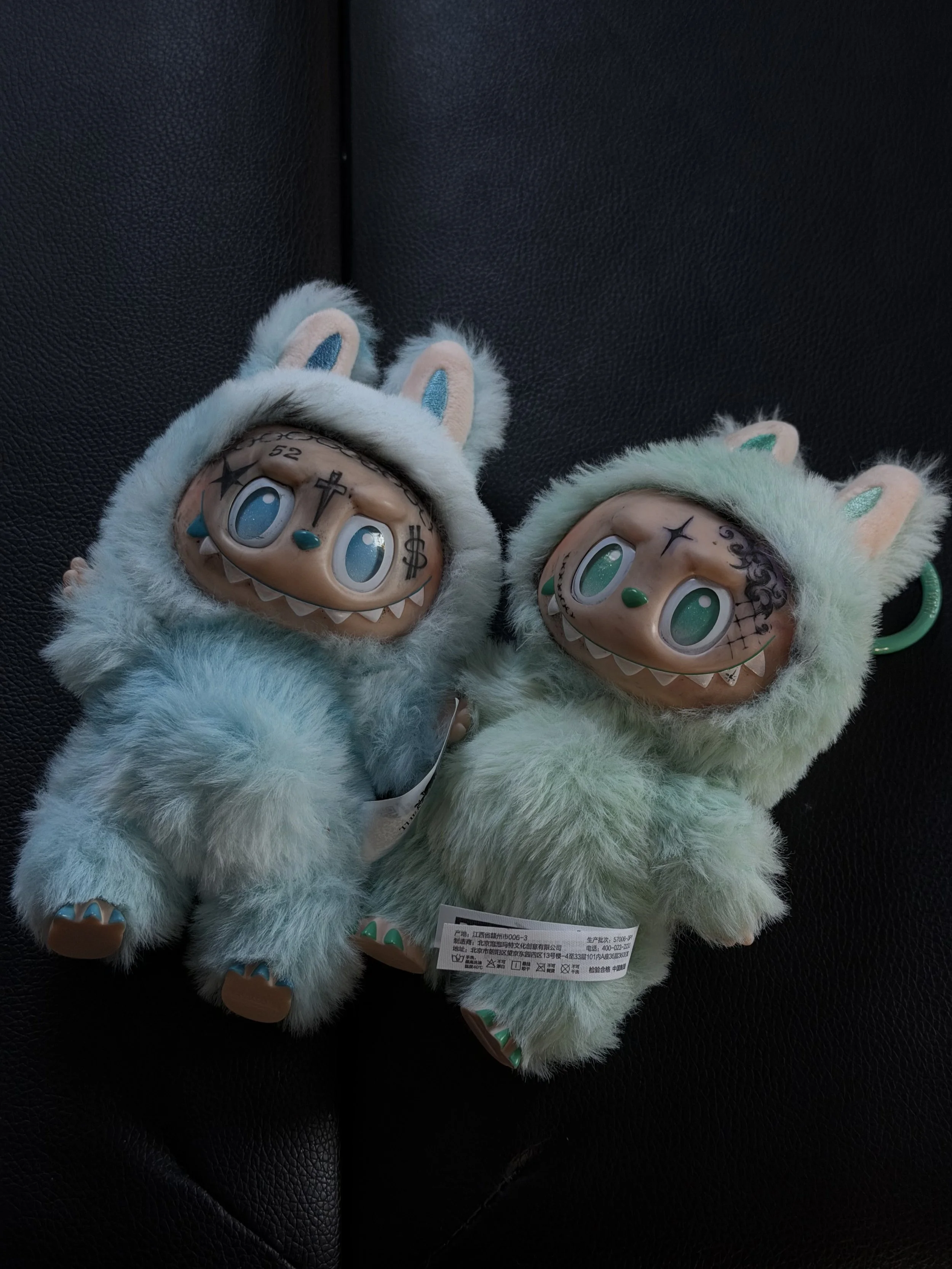 Two Labubu with tattooed faces.