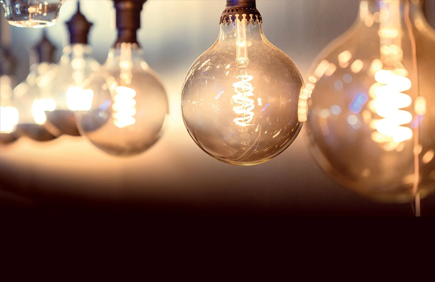 Several glowing vintage-style Edison light bulbs hanging in a row, emitting warm light with visible filaments in a dimly lit setting.