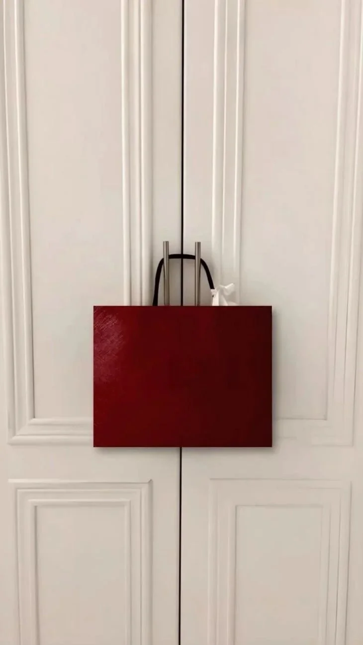A white closet with double doors, a black purse with handles, a white cloth, and a red rectangular object hanging on the door.