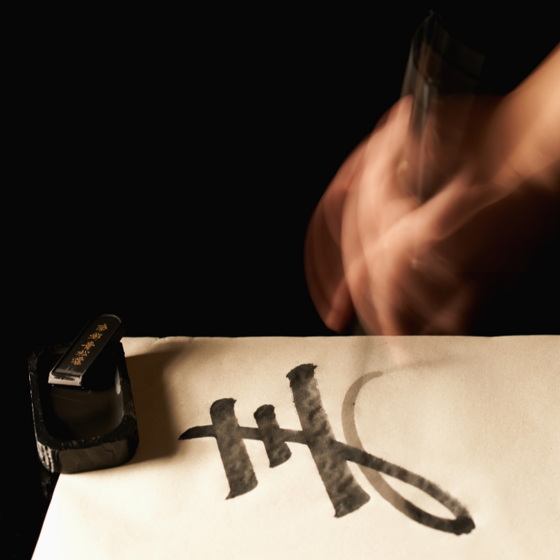 A hand using a brush to write Japanese calligraphy in black ink on paper, highlighting a quiet moment of focus and tradition.