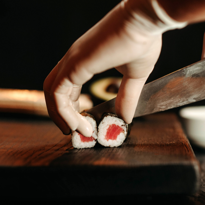 A close-up of sushi being carefully sliced on a wooden board, capturing the precision and ritual of Japanese cuisine.