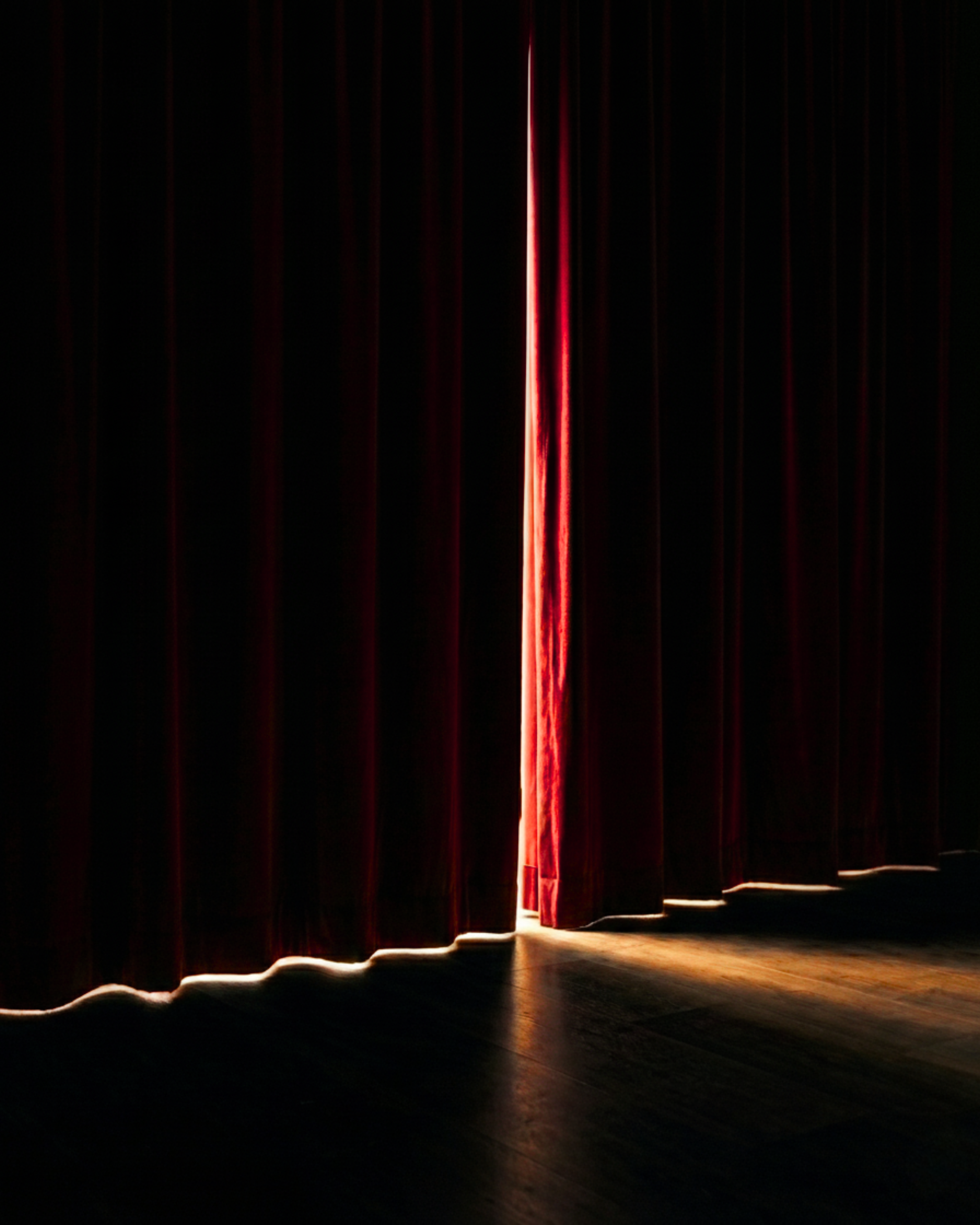 Red stage curtains opening slightly as soft light enters, evoking the feeling of stepping into a story or a moment about to begin.