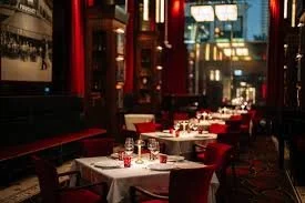 An elegant restaurant dining room prepared for the evening, with red chairs and white tablecloths setting a refined and intimate atmosphere.