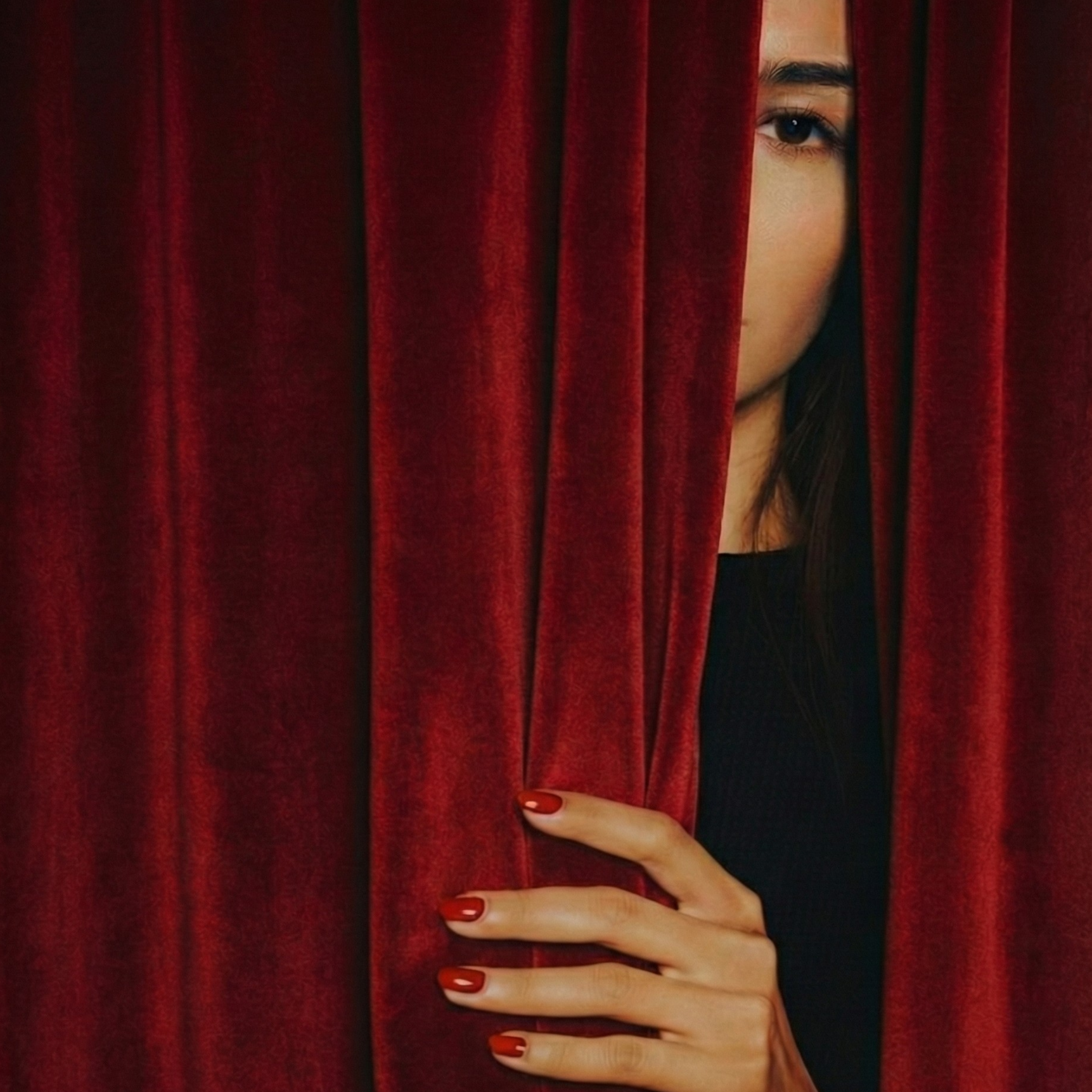 A woman peeking out from behind deep red velvet curtains, creating a sense of mystery, intimacy, and anticipation.