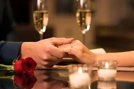 A close-up of a couple's hands holding, captured in candlelight with champagne glasses in the background, marking an intimate and meaningful moment.