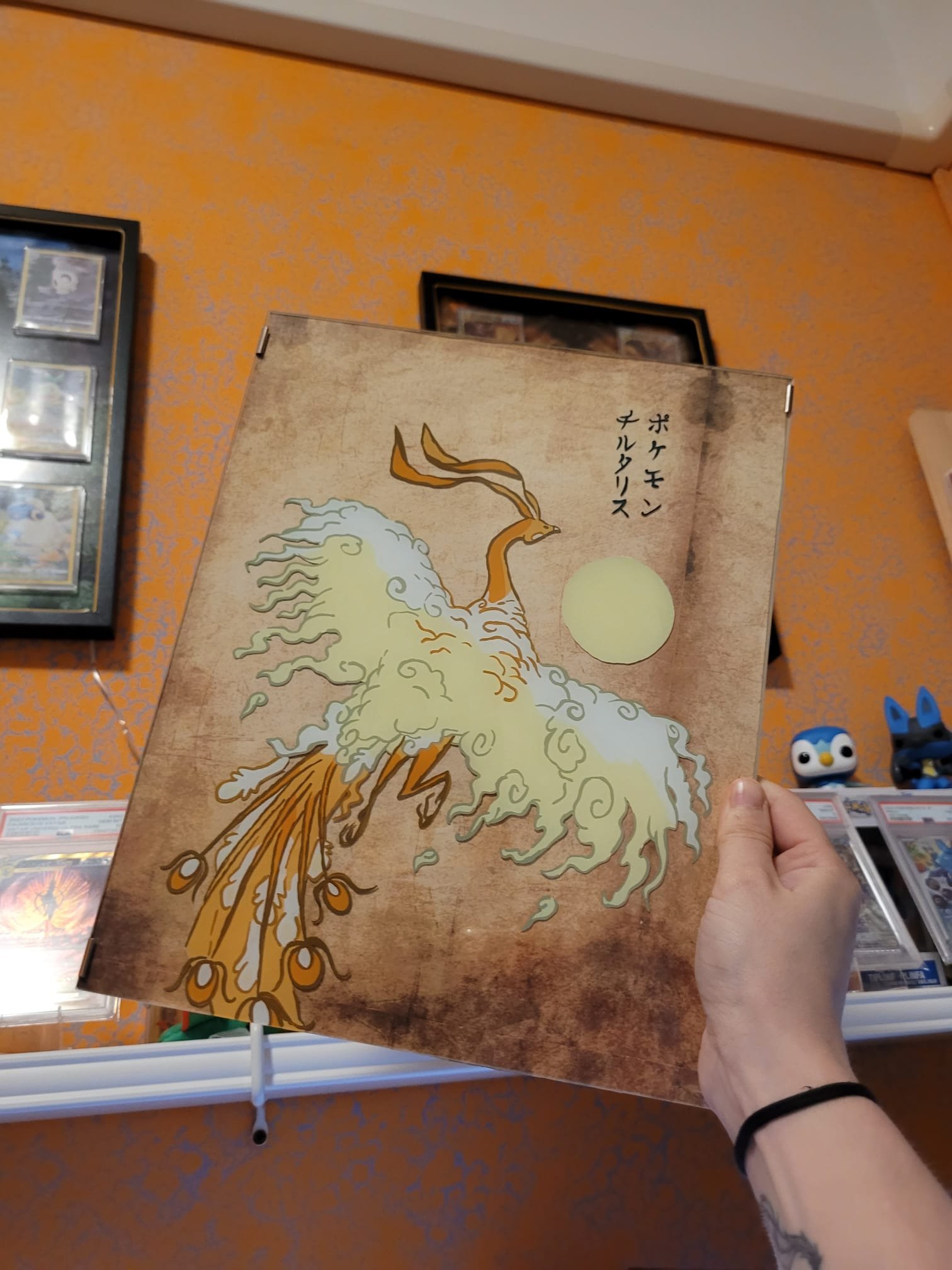Una mano tiene un libro con copertina illustrata del Pokémon Altaria, raffigurato come un uccello con ali luminose, con un cielo di luna piena sullo sfondo.