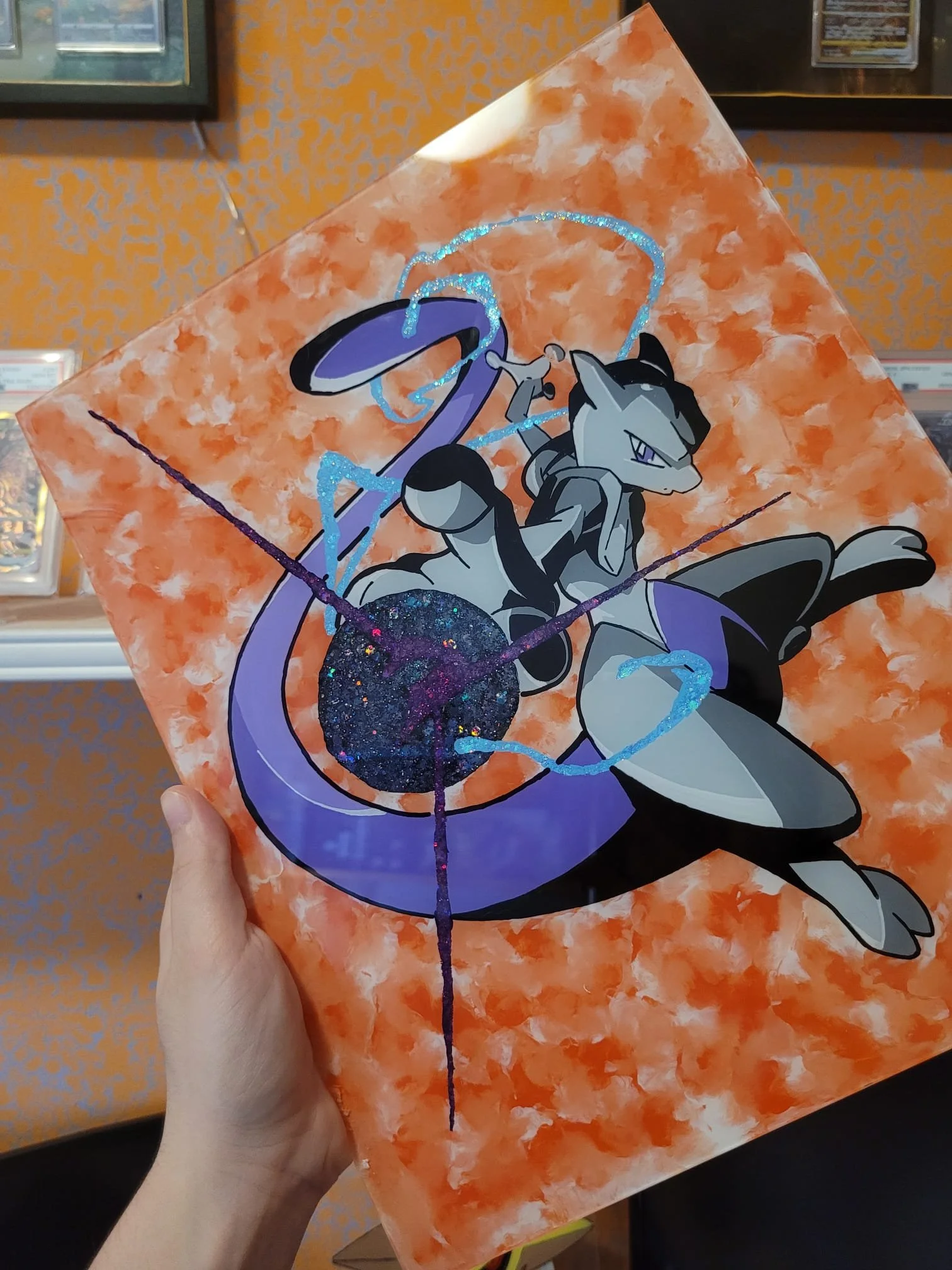 Quadro con immagine del Pokémon Mew Two, su uno sfondo arancione con dettagli blu e glitter.
