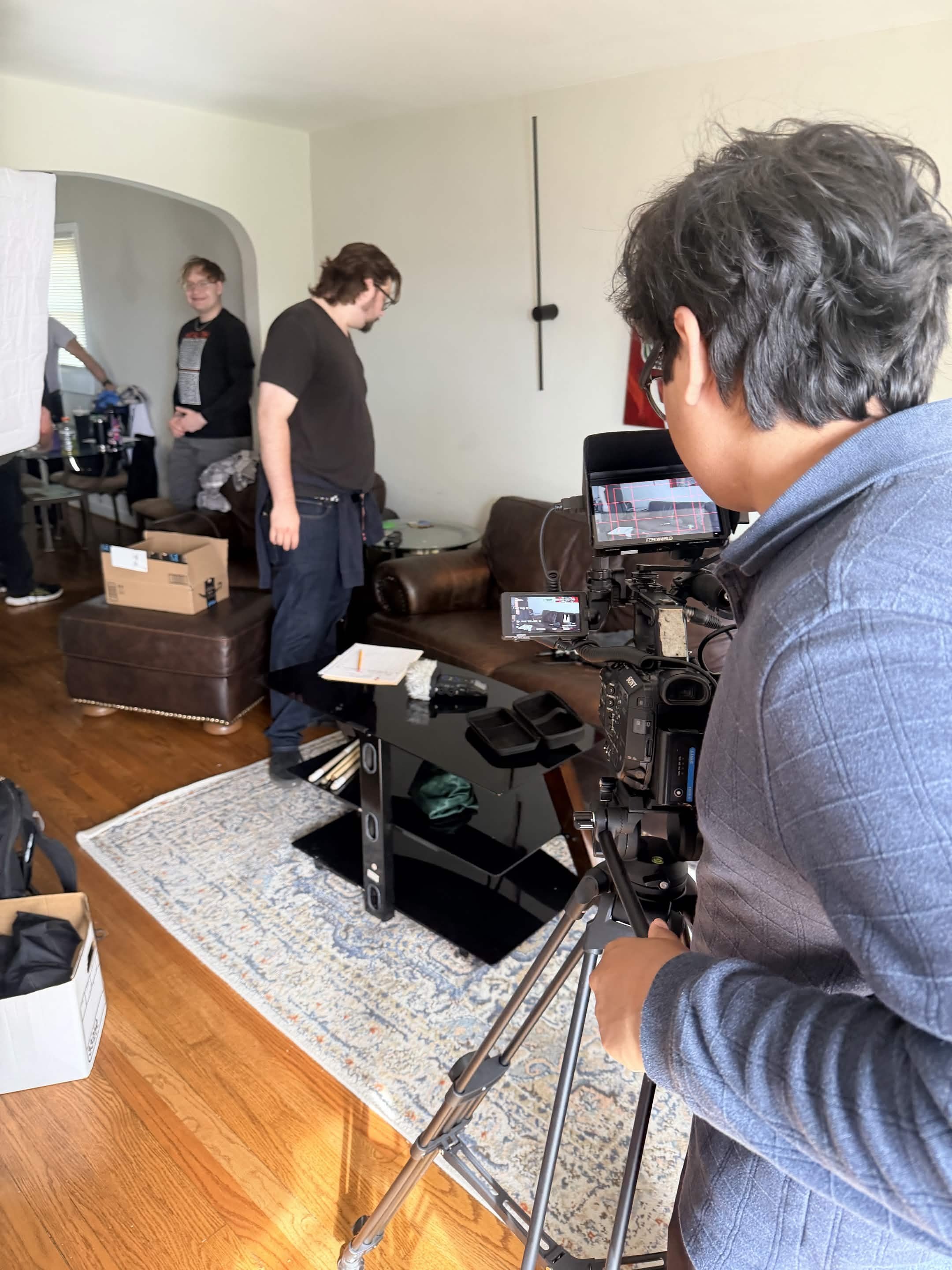 People on a film or photo shoot set in a living room, with camera equipment and crew members preparing for a shoot.