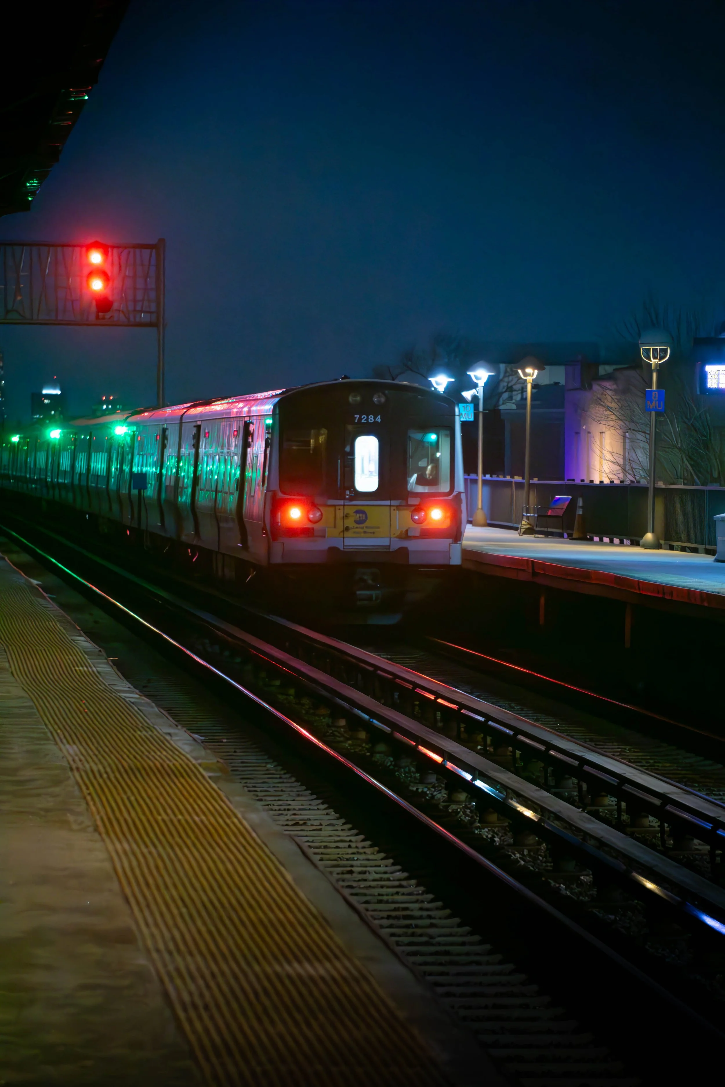 A light rail train arriving at a station during nighttime, illuminated by streetlights and signals.
