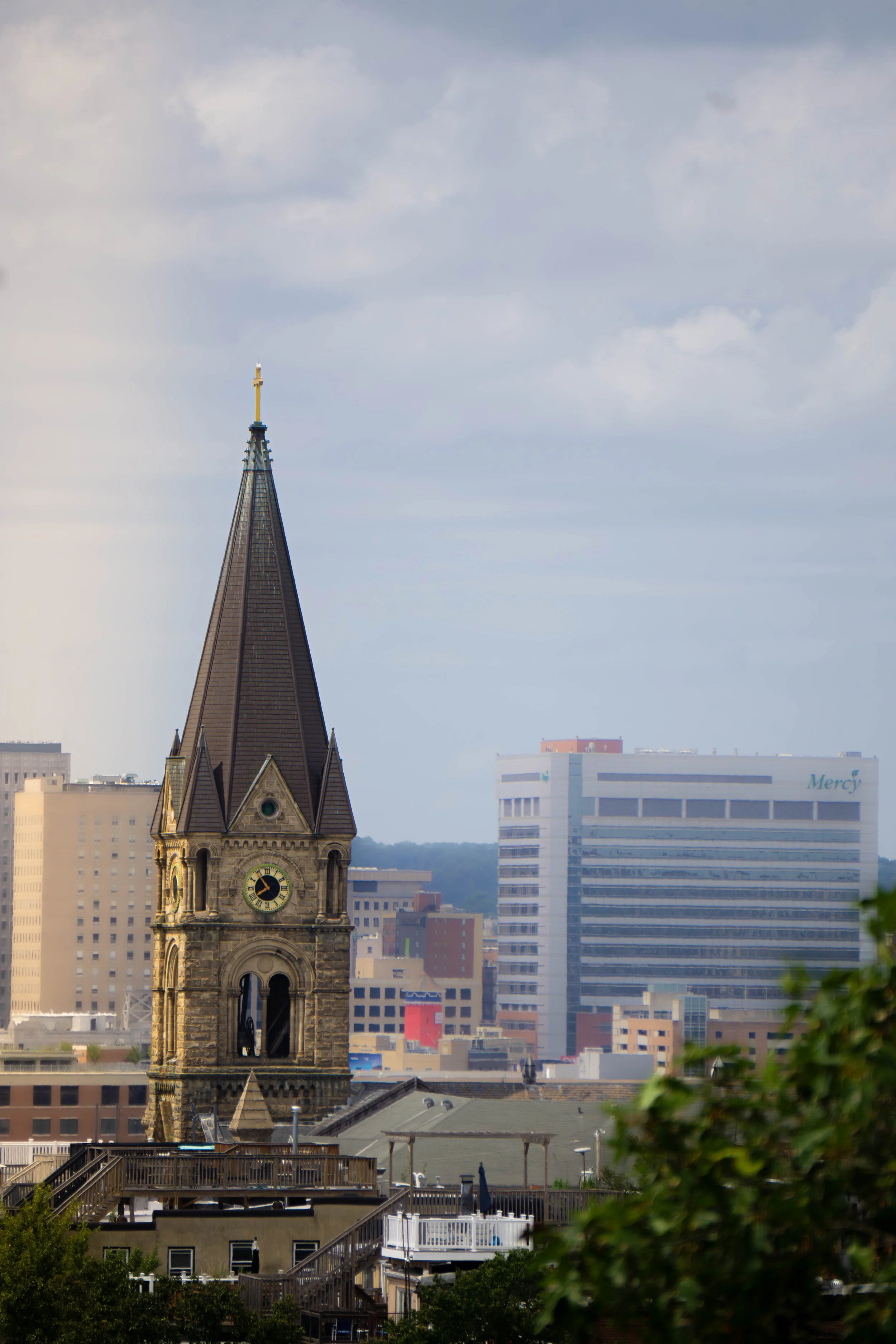 Cityscape featuring a historic church with a tall steeple and clock, surrounded by modern office buildings under a cloudy sky.