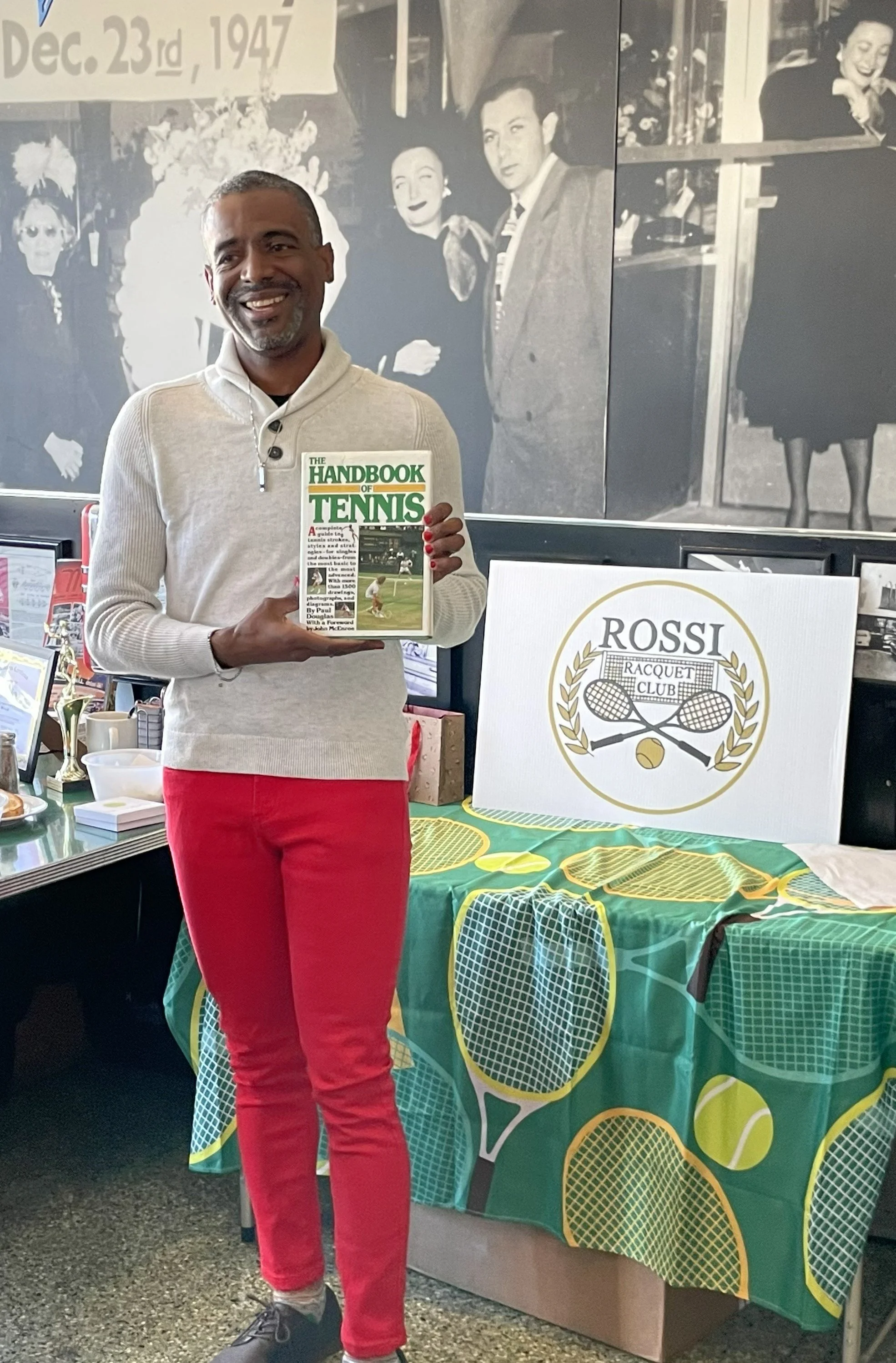 Rossi Racquet Club founder Chad M. holding 'The Handbook of Tennis' at Rossi Racquet Club holiday breakfast event at Mel's Diner