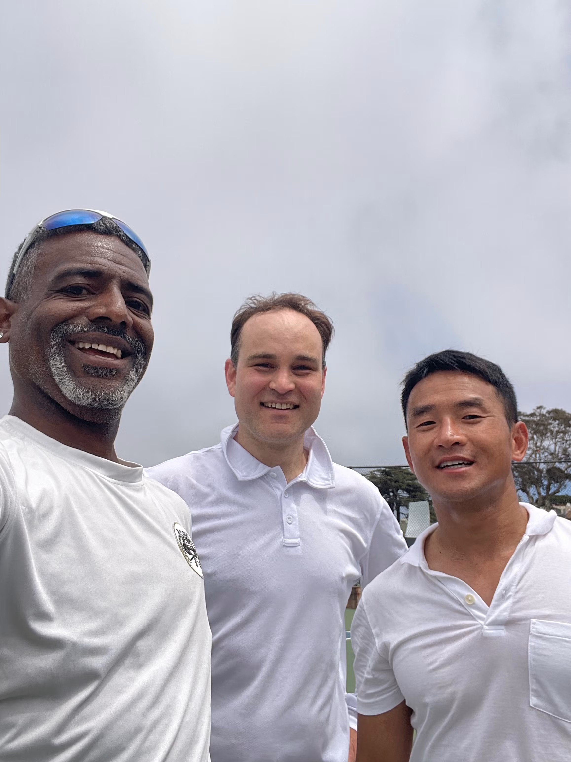 Three Rossi Racquet Club members smiling outdoors at tennis courts