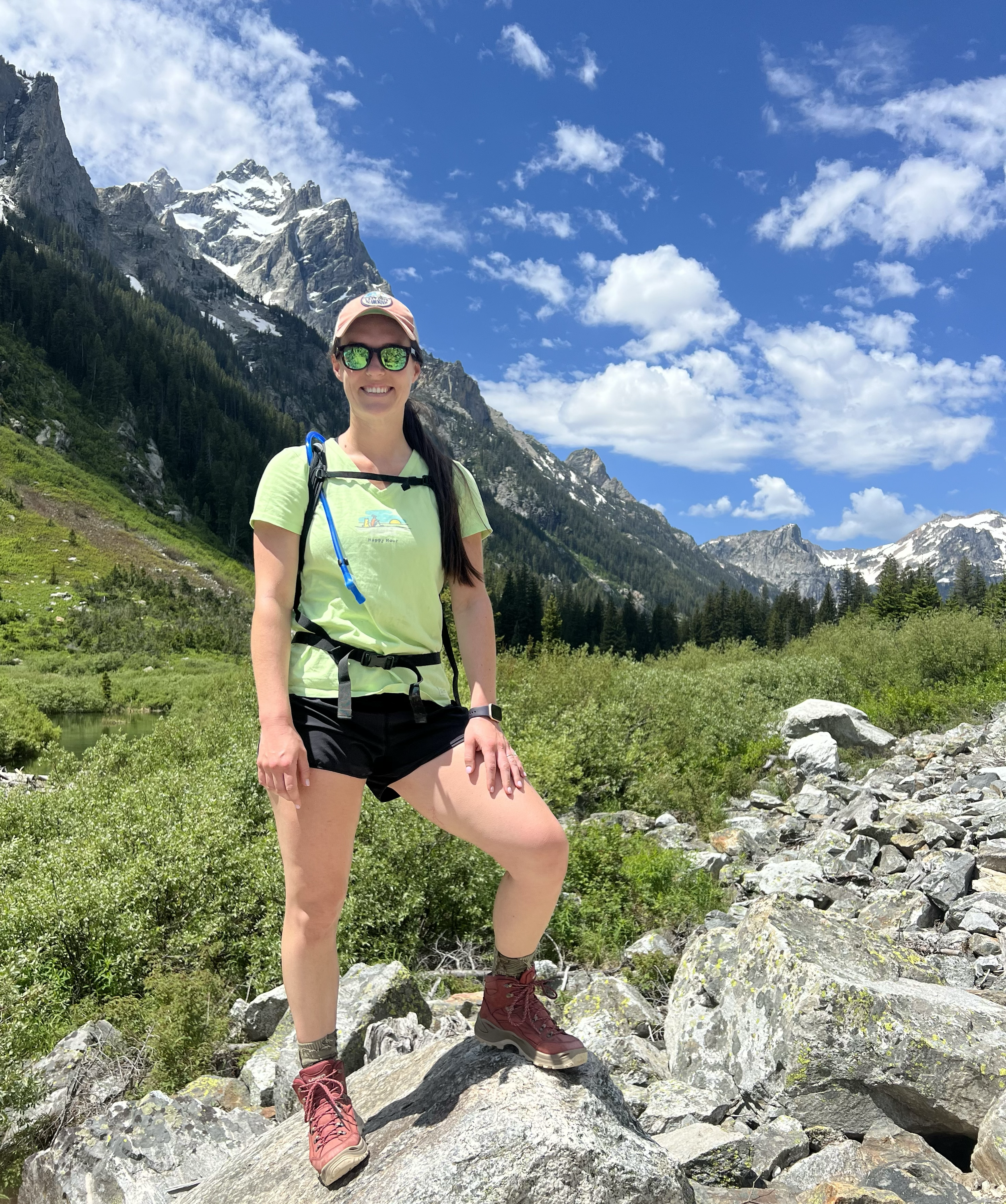 A woman hiking outdoors on rocky terrain with mountains and a blue sky with clouds in the background.