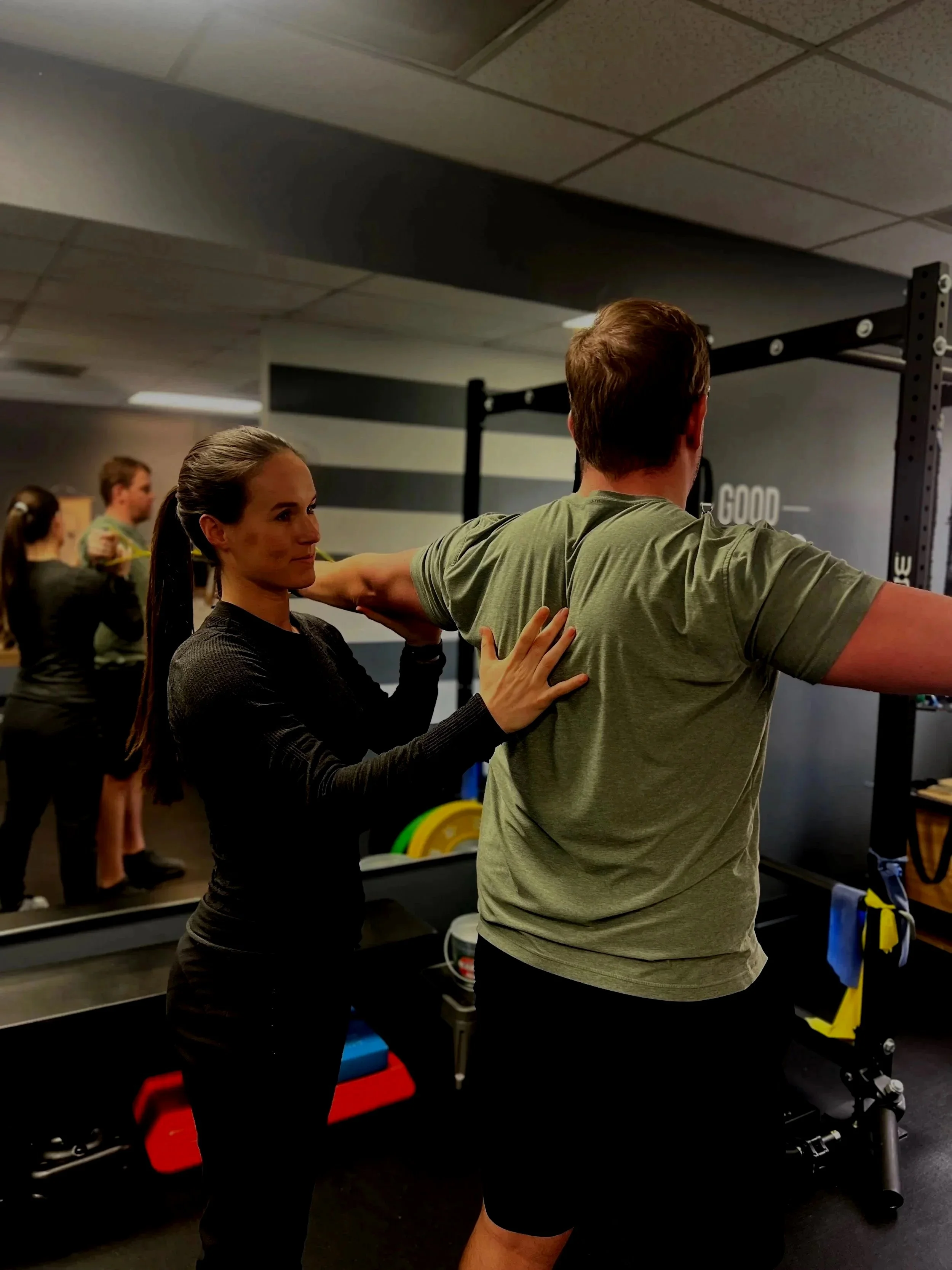 Personal trainer assisting a man with shoulder exercises in a gym.
