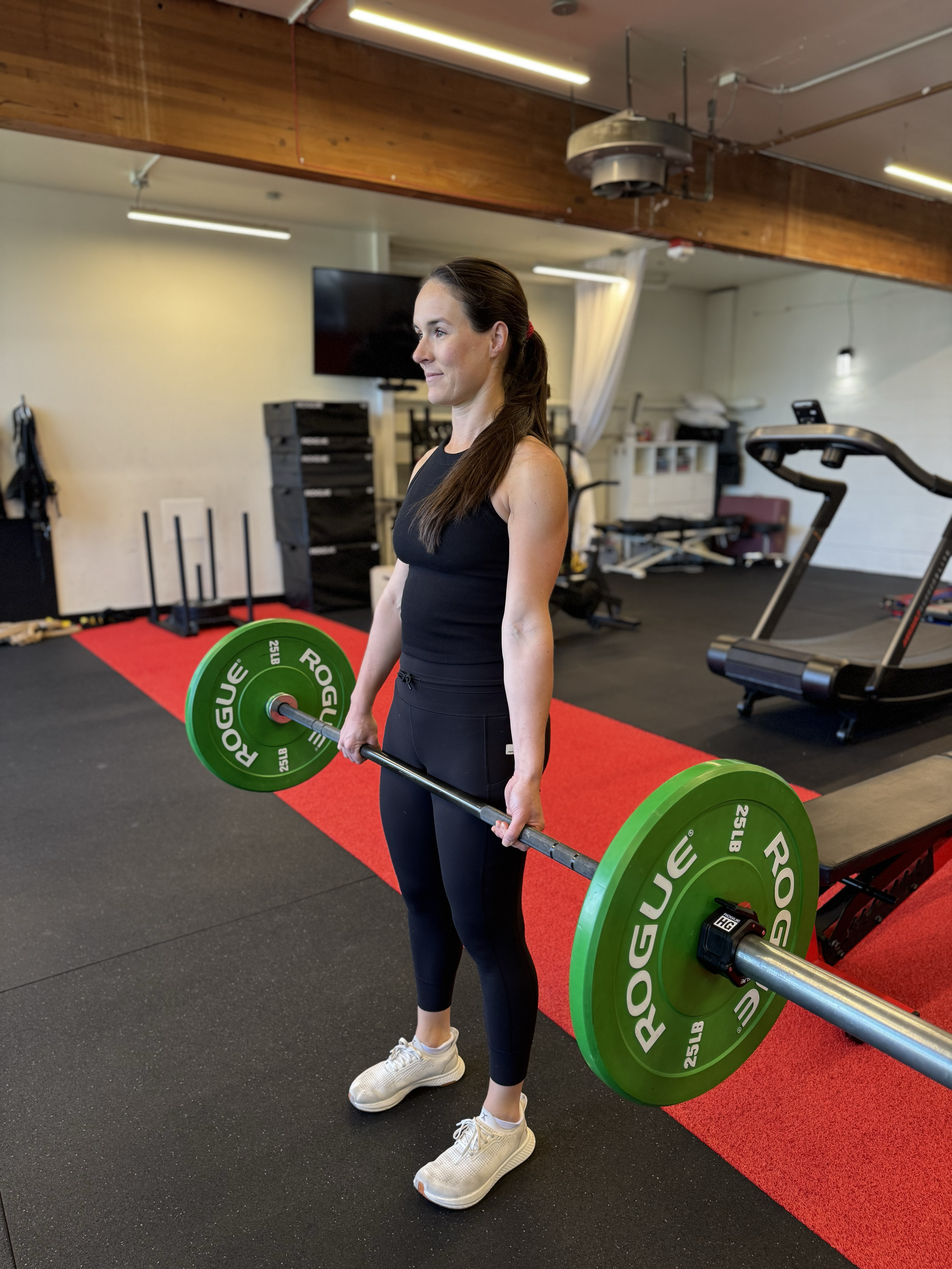 Woman lifting a green barbell with weights in an indoor gym.