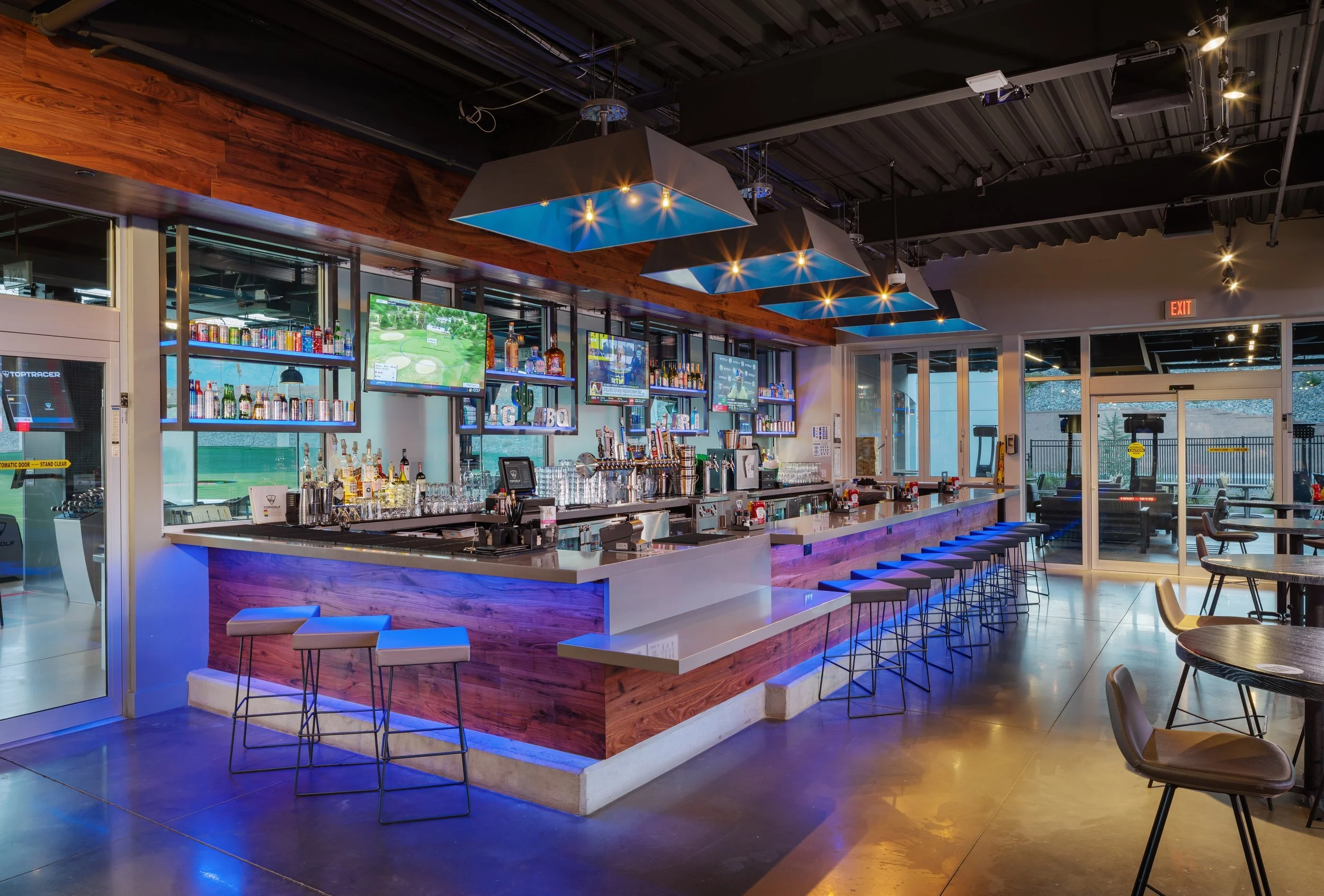 Sports bar with wooden accents, multiple TV screens showing golf games, and a long bar counter with barstools.