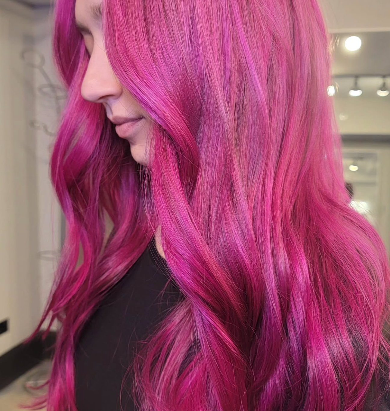 Woman with long, wavy, pink hair in a salon setting.