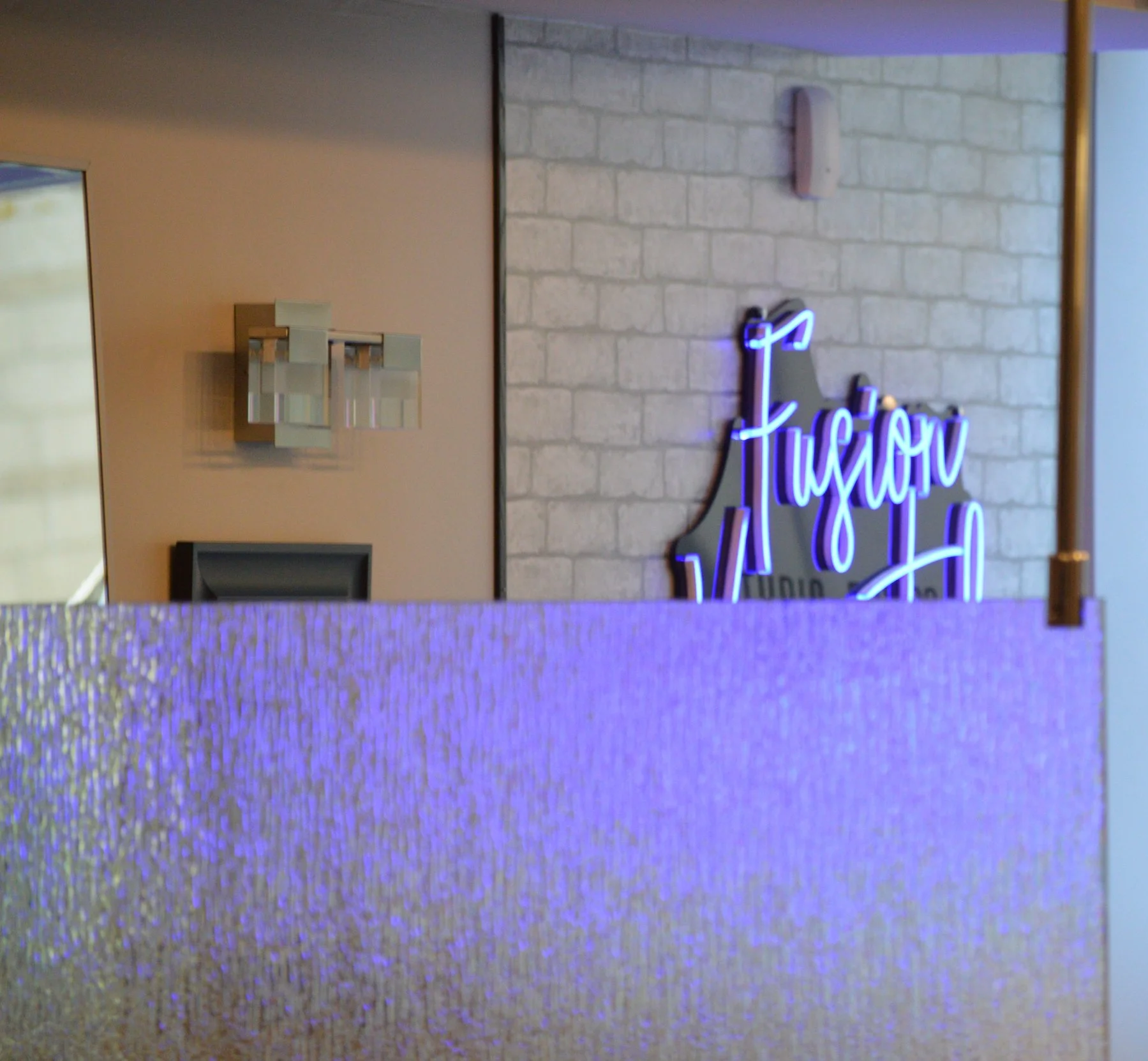 Interior of a business with a purple neon sign that reads 'Fusion' on a brick wall, partly obscured by a textured purple partition.