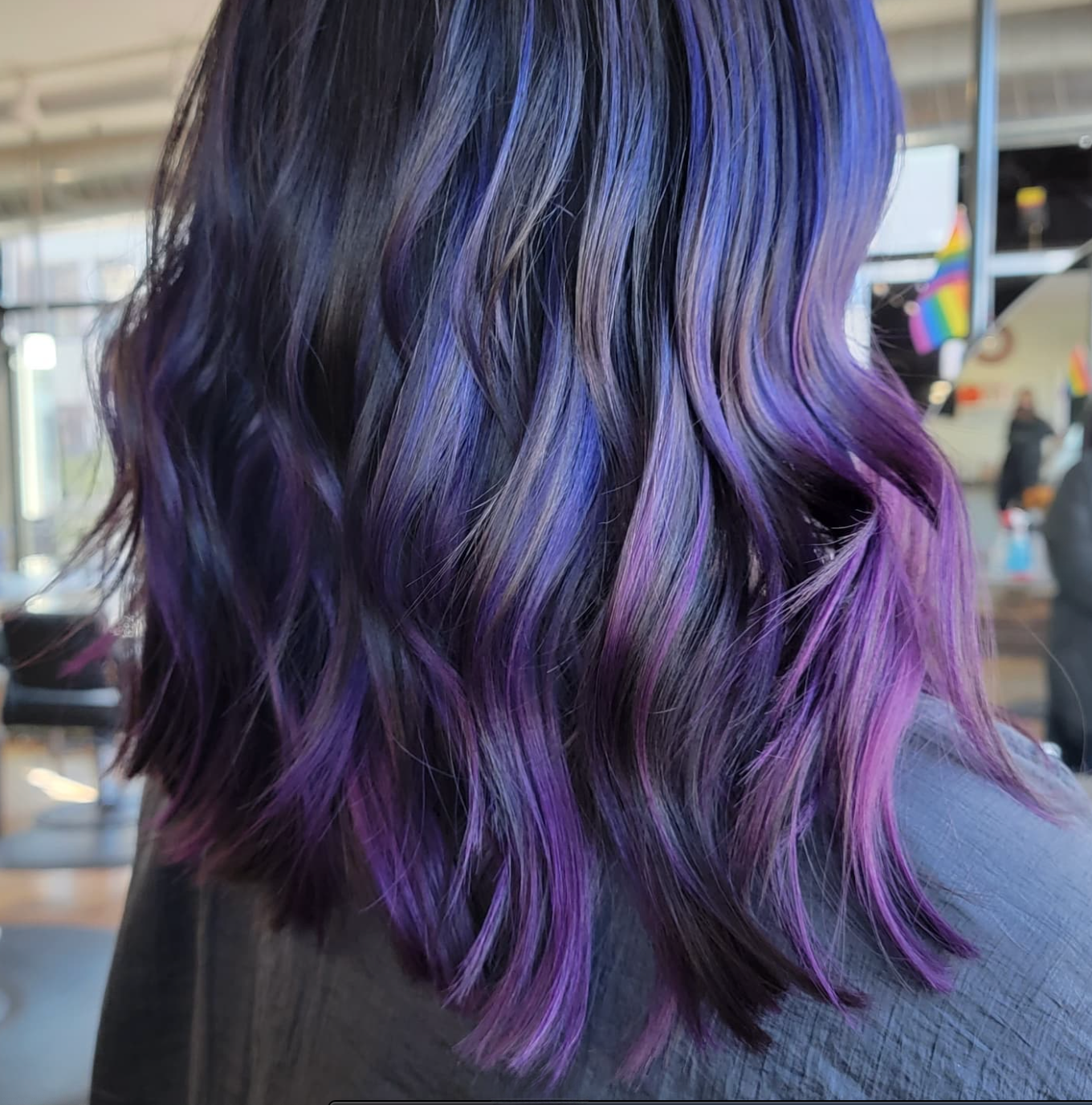 Close-up of a woman's wavy hair dyed in shades of purple and blue in a salon setting.