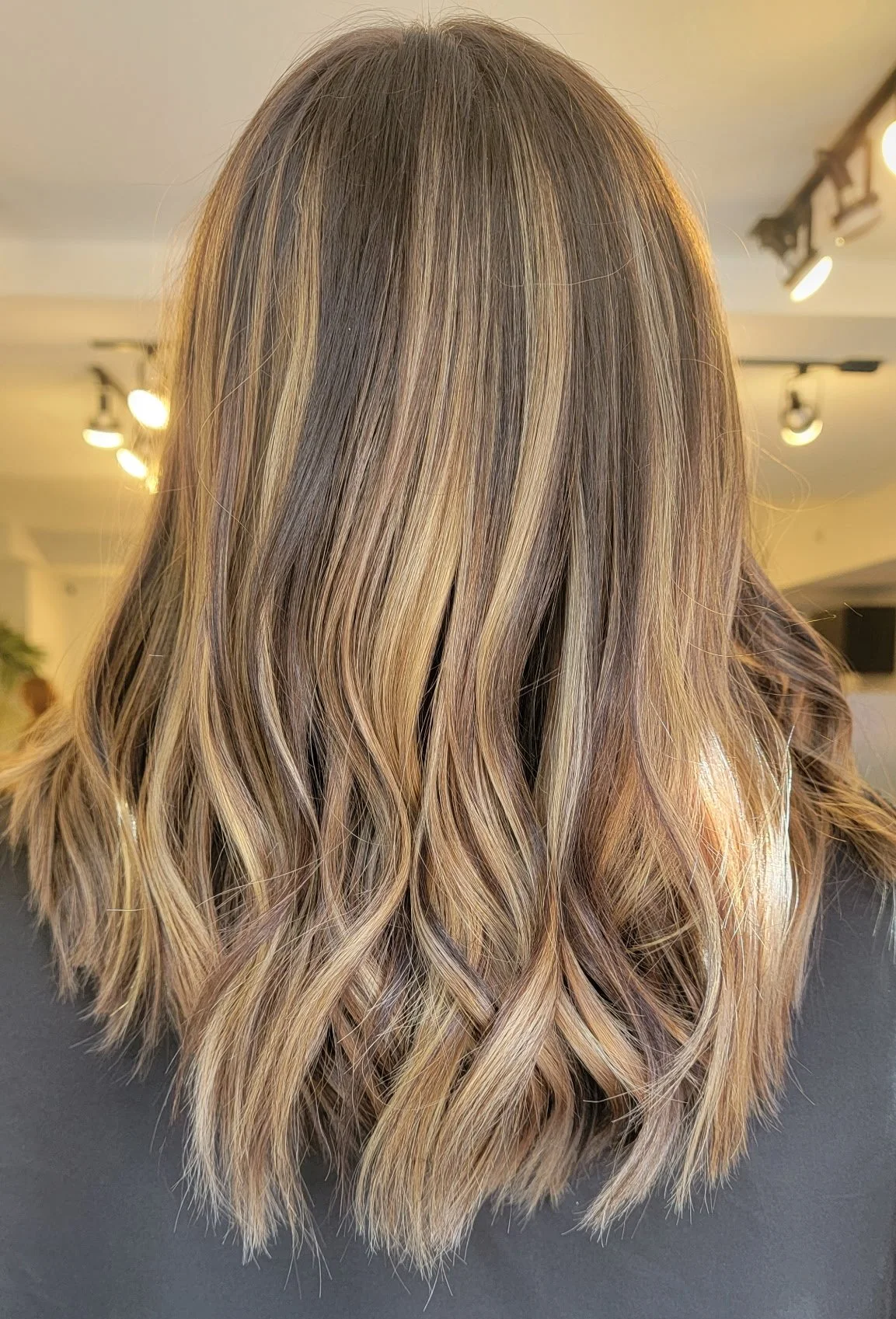 Back of woman with shoulder-length, wavy, blonde hair with darker roots.
