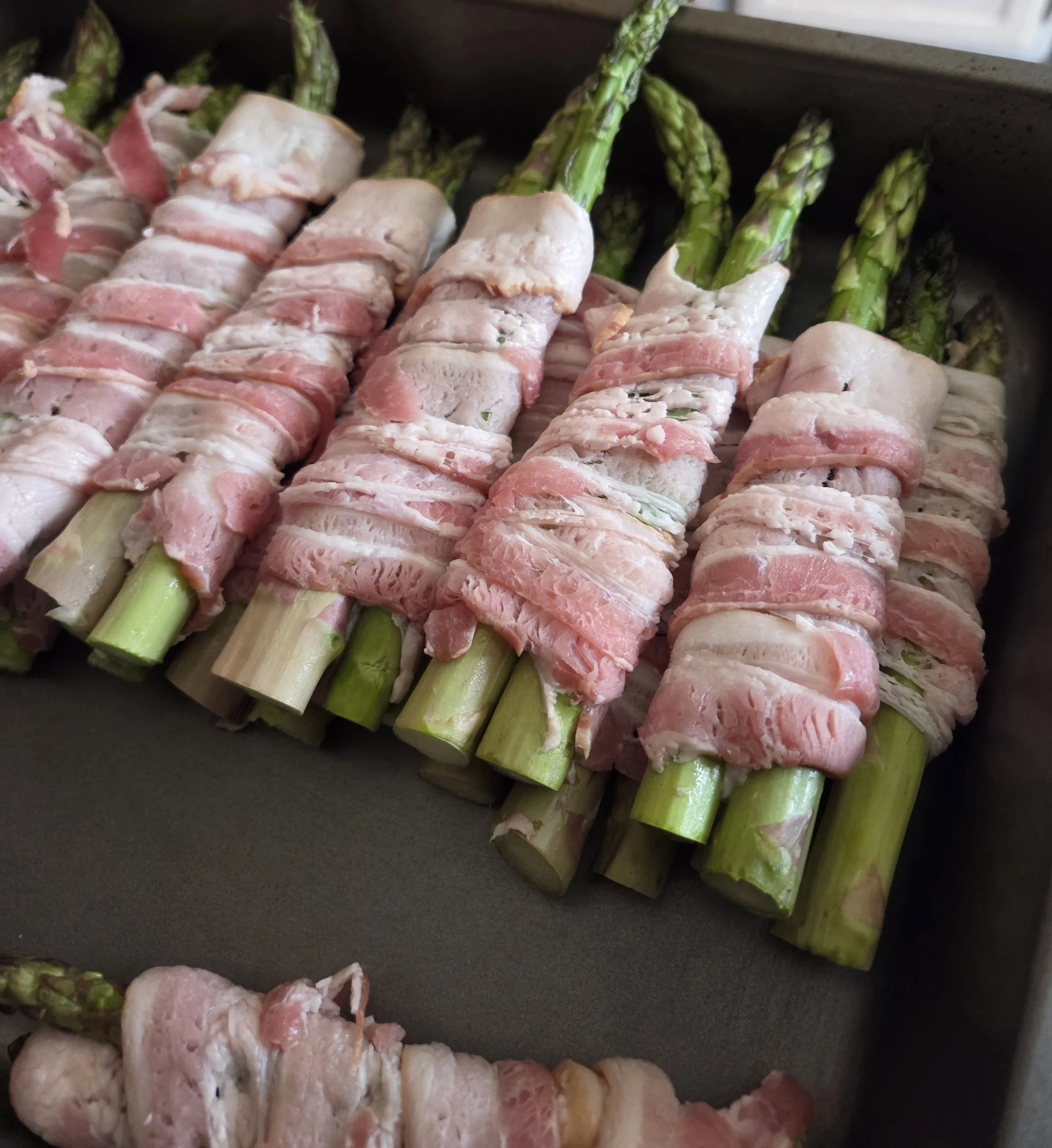 Bacon-wrapped asparagus in a baking tray.