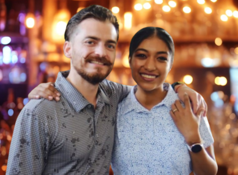 A man and a woman smiling and posing together in a warmly lit bar or restaurant.