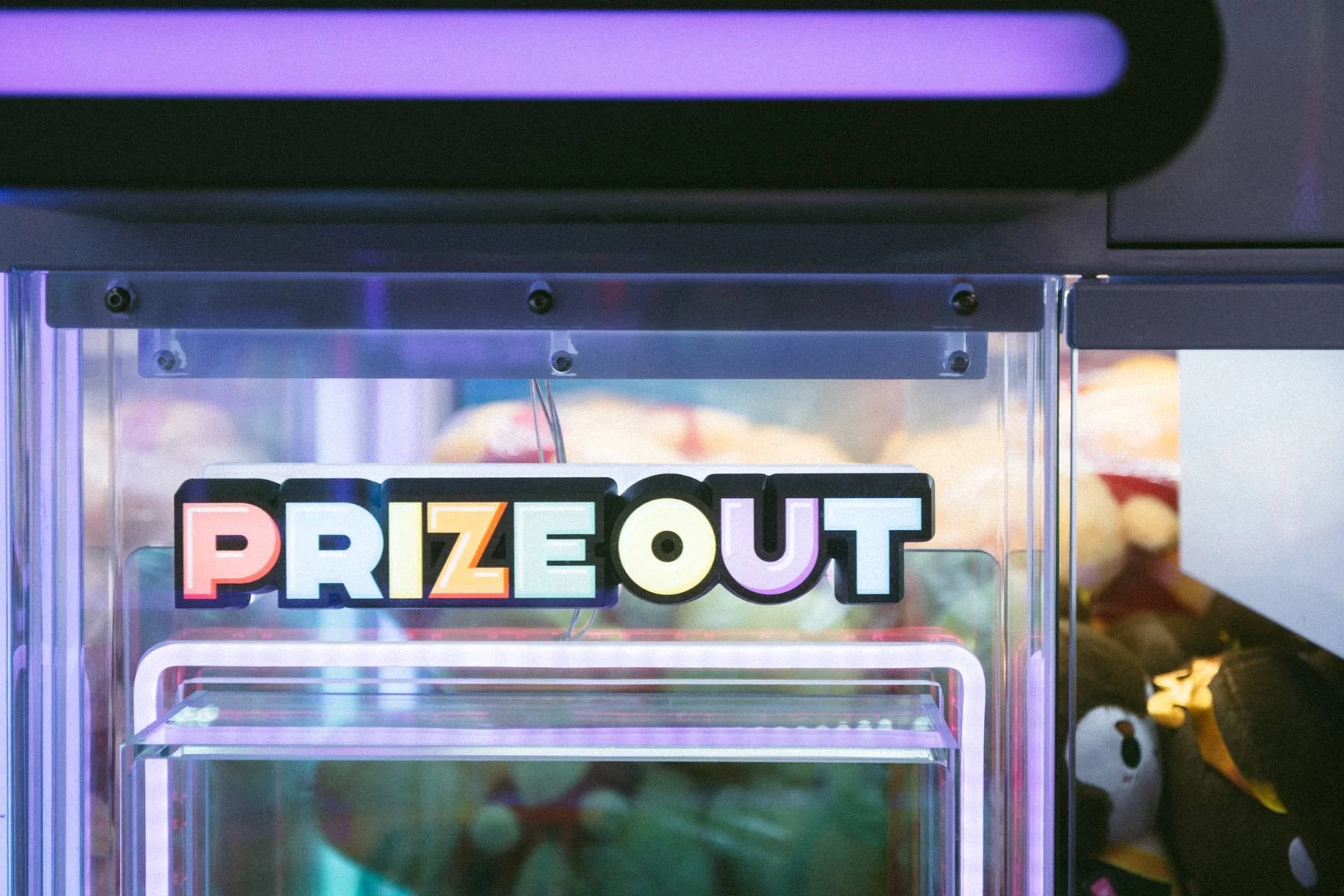 Colorful sign that reads 'PRIZE OUT' inside an arcade claw machine with plush toys inside.